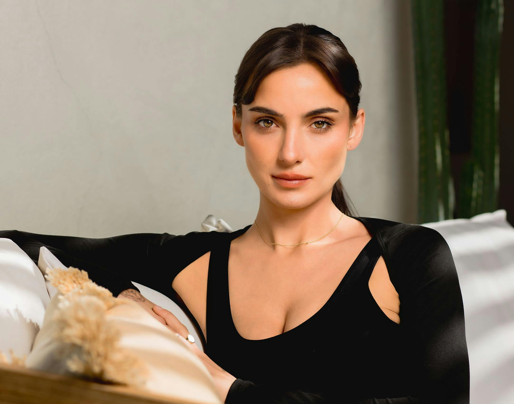 black haired woman sitting on couch with arm on pillow