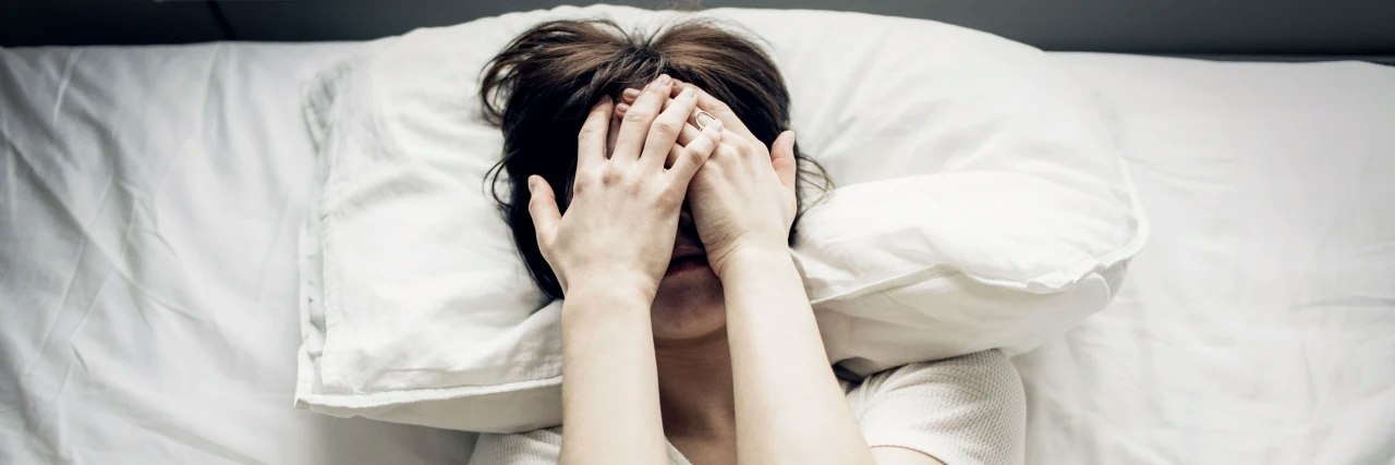 Frau im Bett mit Händen vor dem Gesicht