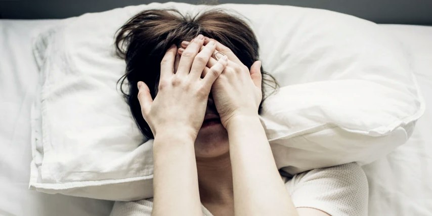 Frau im Bett mit Händen vor dem Gesicht Frau im Bett mit Händen vor dem Gesicht