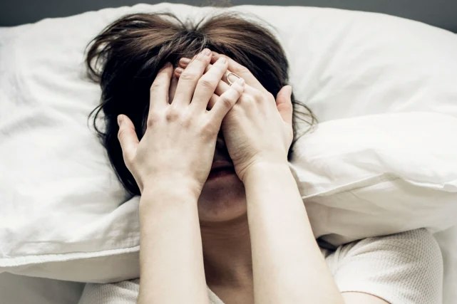 Frau im Bett mit Händen vor dem Gesicht Frau im Bett mit Händen vor dem Gesicht