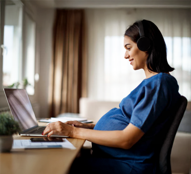 Smiling pregnant woman sitting in front of a laptop and wearing headphones
