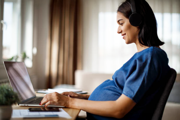 Schwangerschaft Wissen Bild Smiling pregnant woman sitting in front of a laptop and wearing headphones