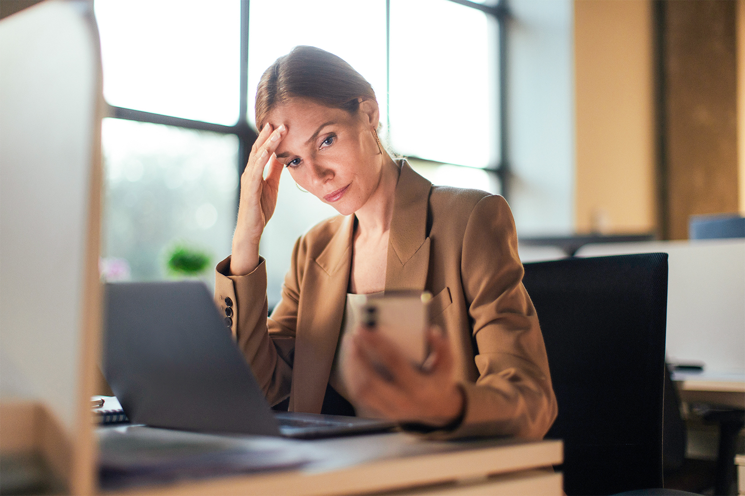 Frau im Büro am Laptop und schaut ins Handy Frau im Büro am Laptop und schaut ins Handy