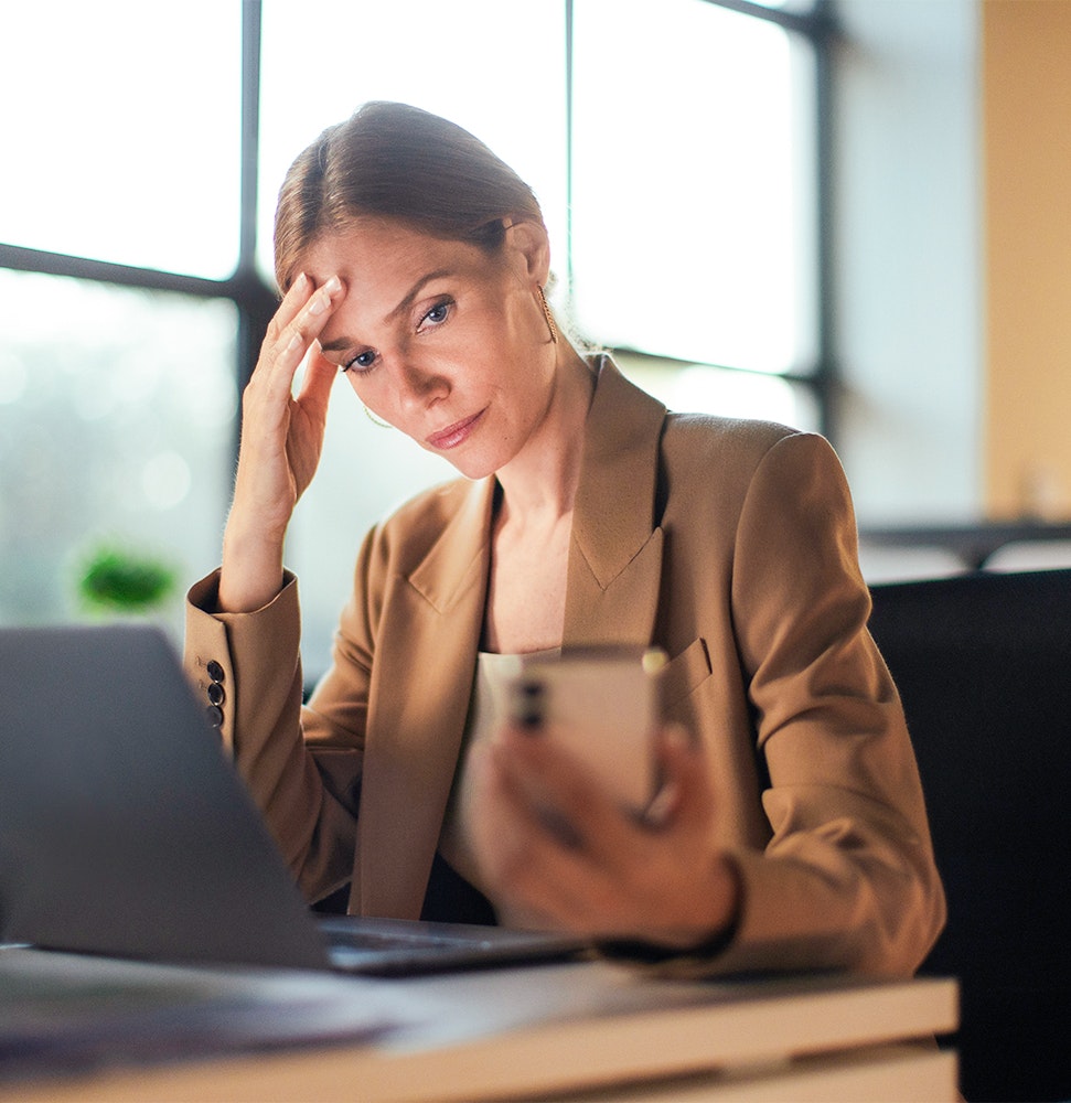 Frau im Büro am Laptop und schaut ins Handy Frau im Büro am Laptop und schaut ins Handy