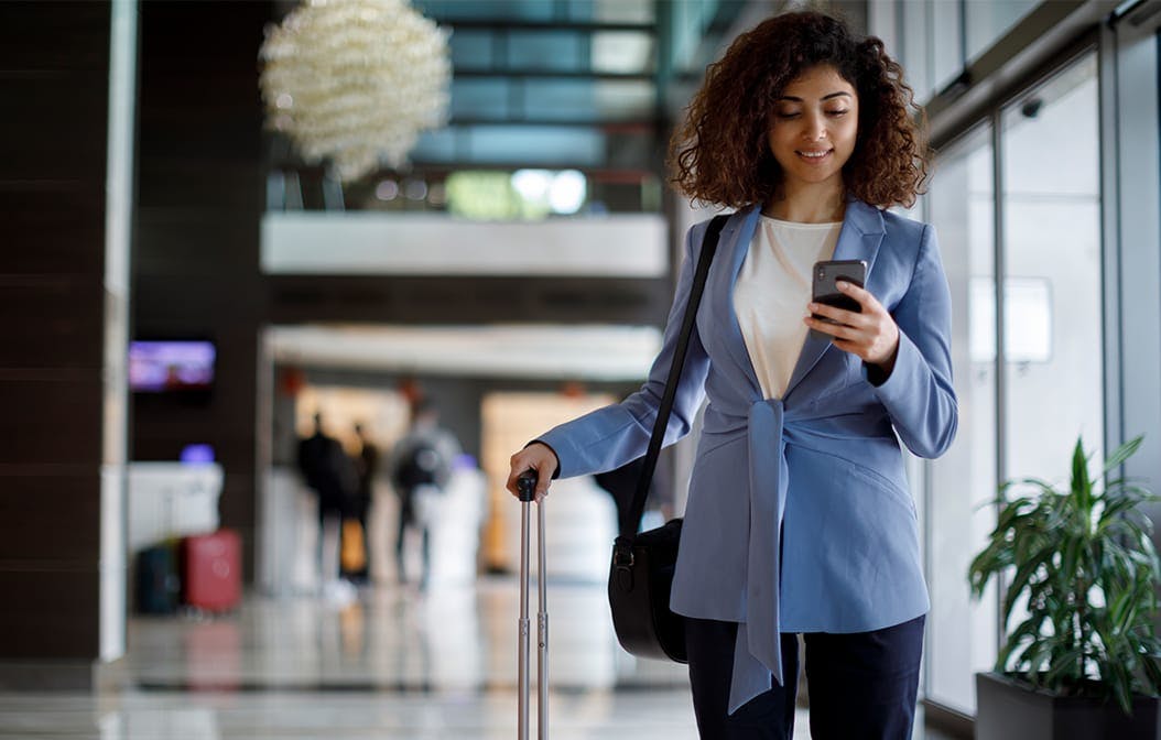 woman walking a roller suitcase, looking at her phone