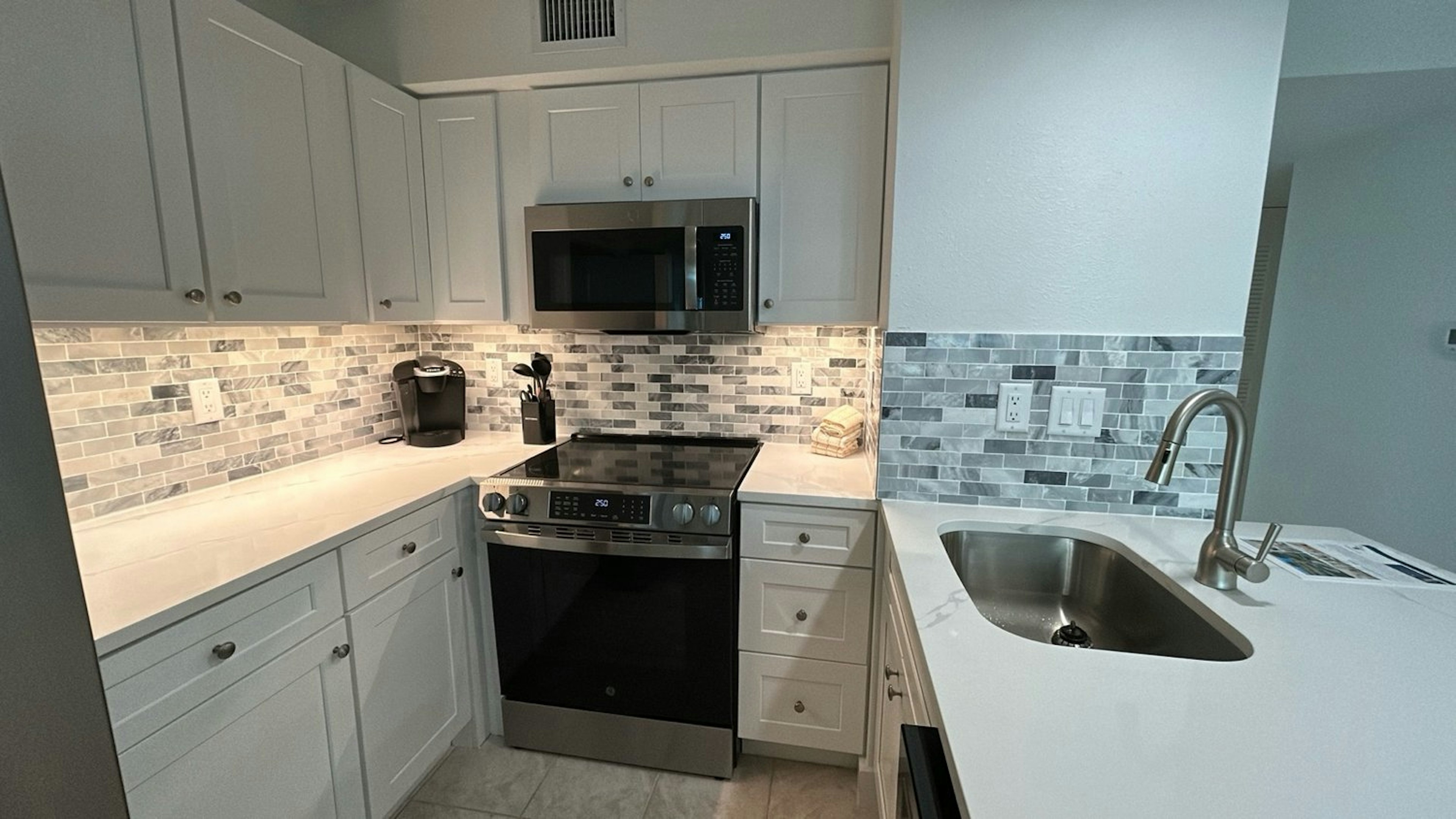 Cook your favorite meals in this sleek, fully-equipped kitchen featuring white cabinets, modern appliances, and elegant tile backsplash.
