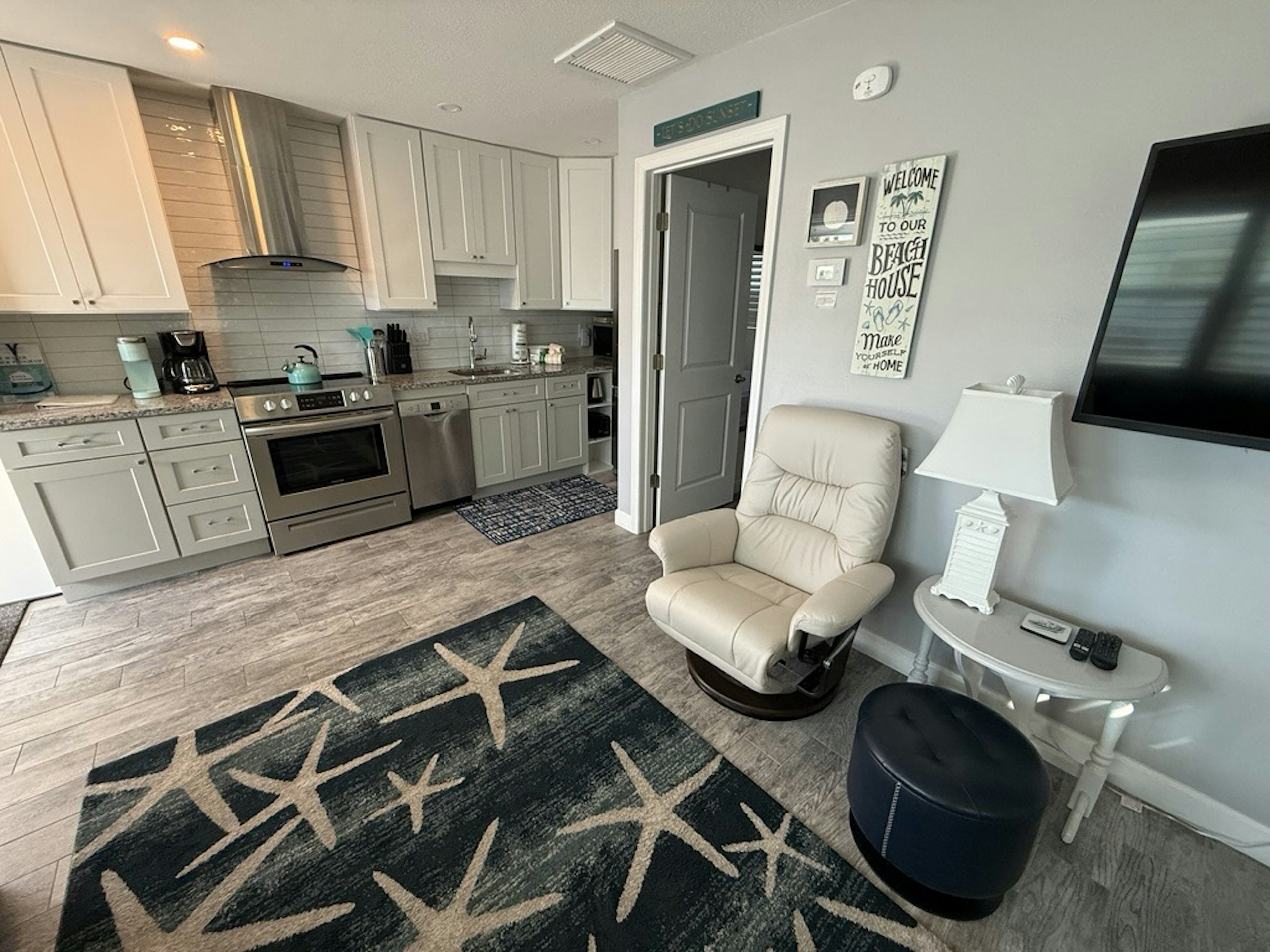 Relax in your open-concept space where modern kitchen meets cozy living area, complete with comfortable seating and beach-themed touches.