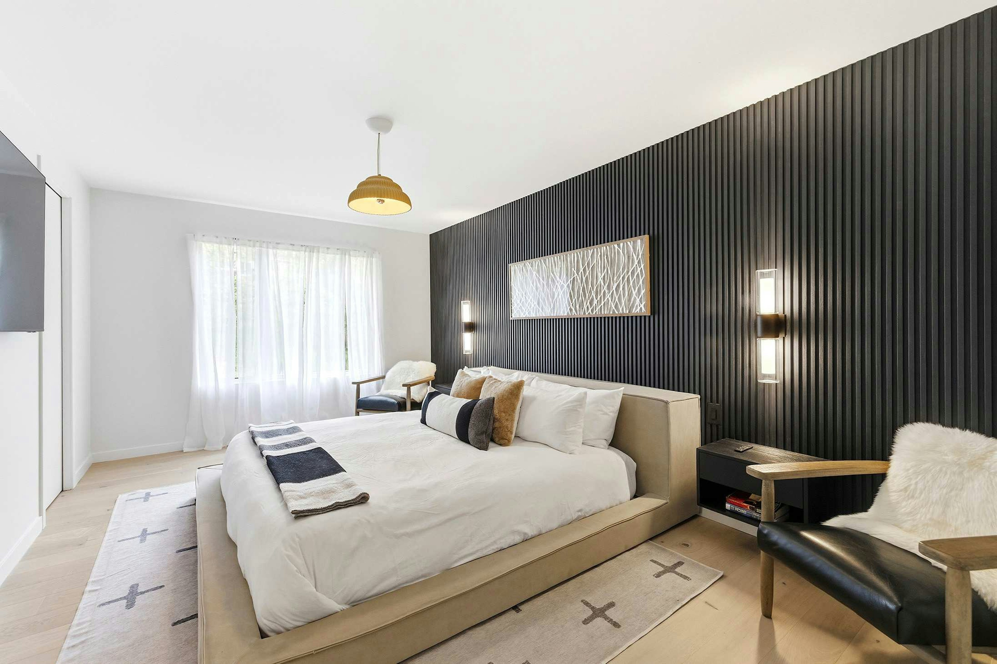 Crisp white linens and warm natural wood meet a bold charcoal slat wall in this contemporary primary bedroom.
