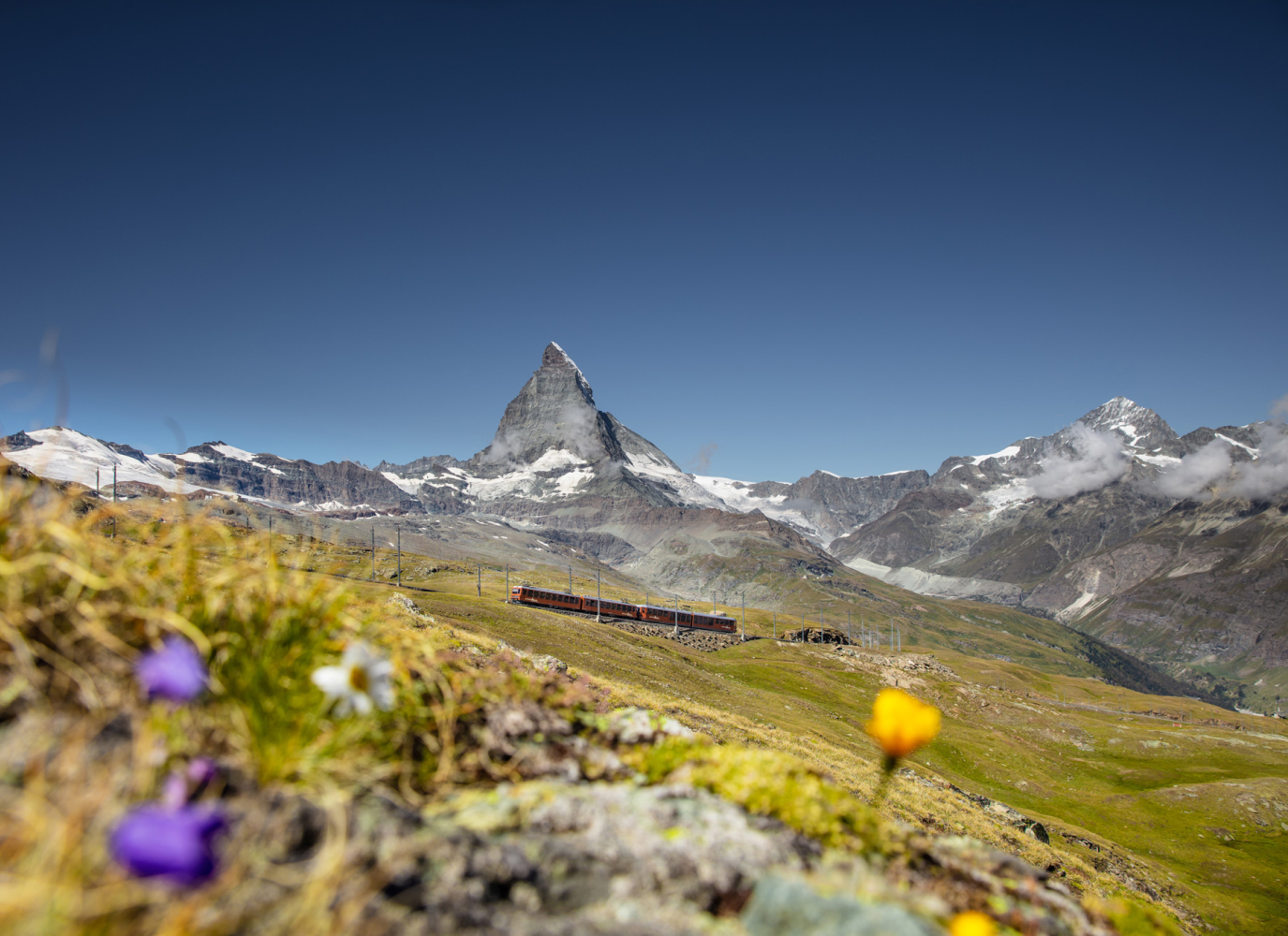Red Gornergrat Railway train climbing alpine tracks with the Matterhorn rising behind