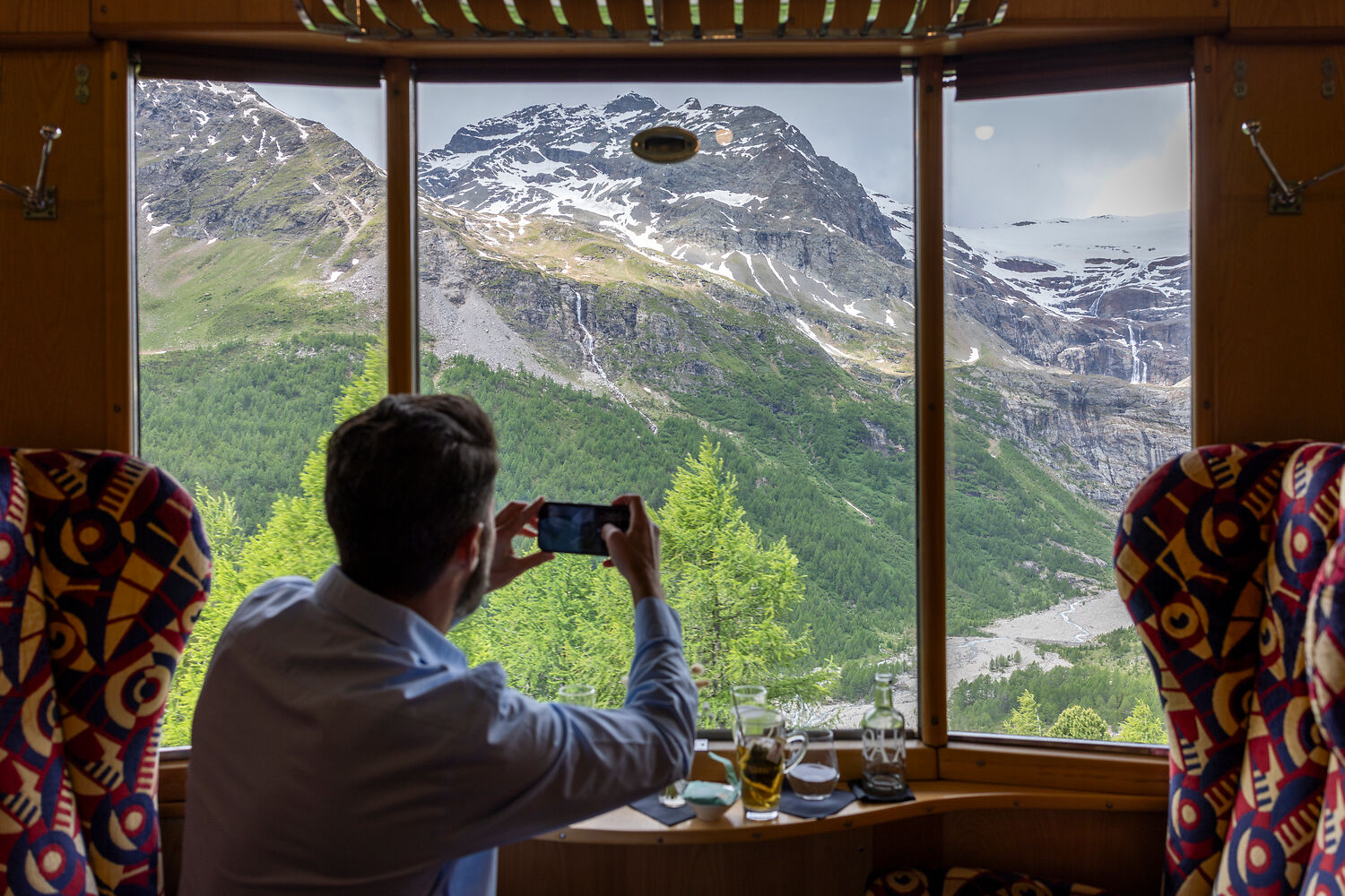 NICOLA PITARO Man sitting in Bernina Express Pullman Class taking picture out of the window into landscape