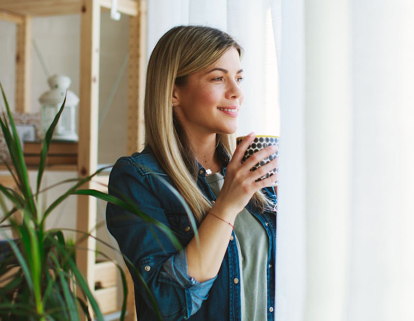 woman standing by window holding a mug smiling