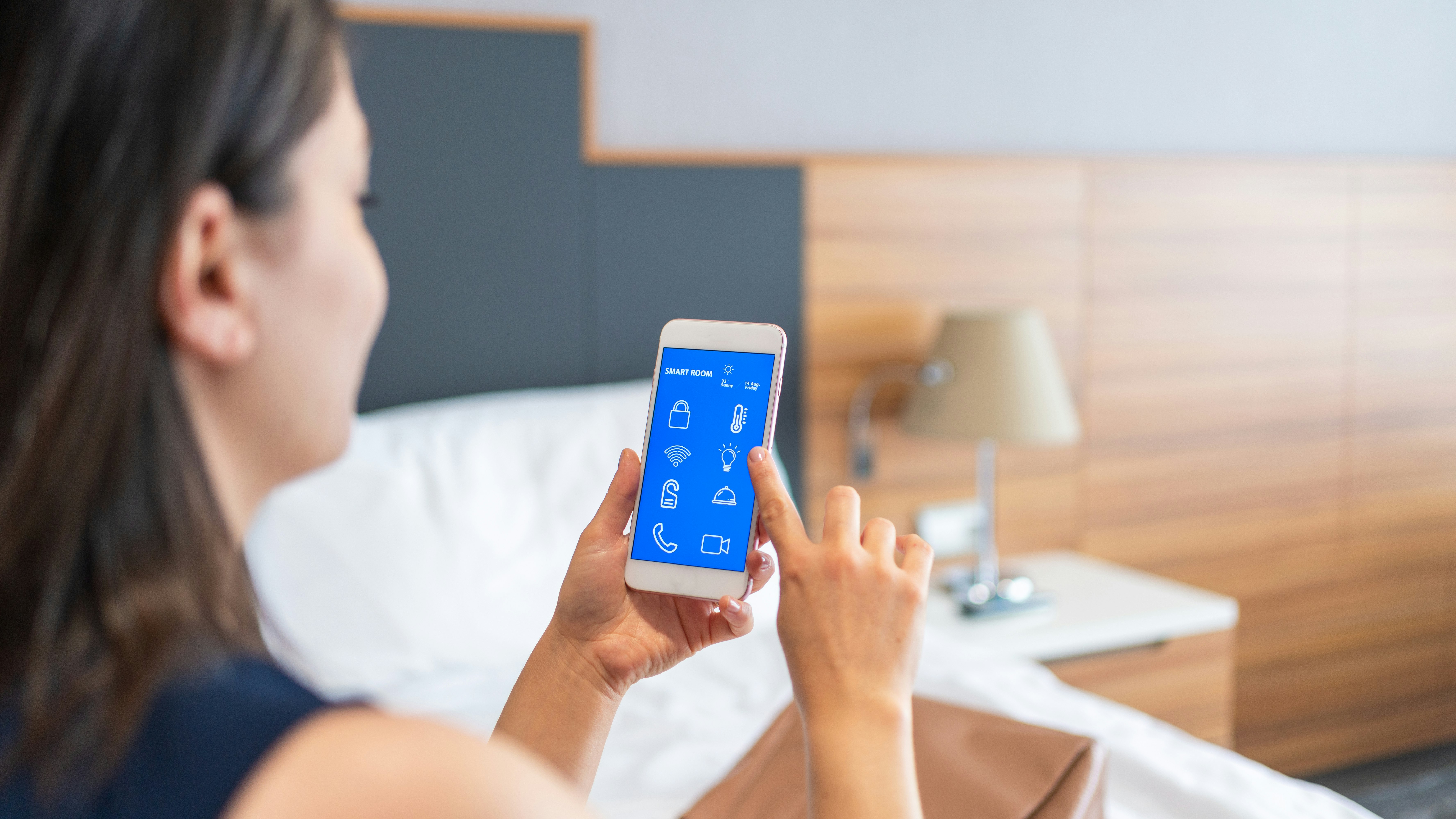 Frau mit Smartphone steuert Smart Room im Schalfzimmer.