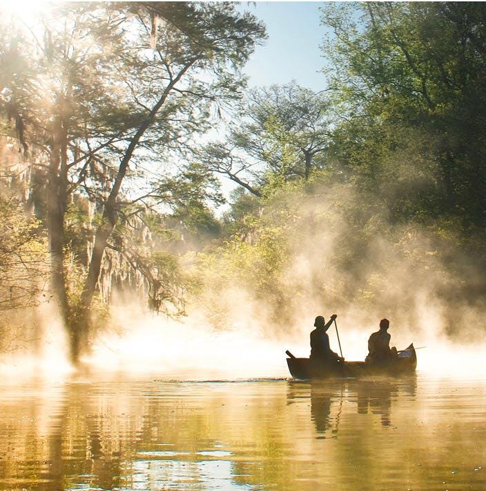 two people on a canoe in the middle of a lake full of mist