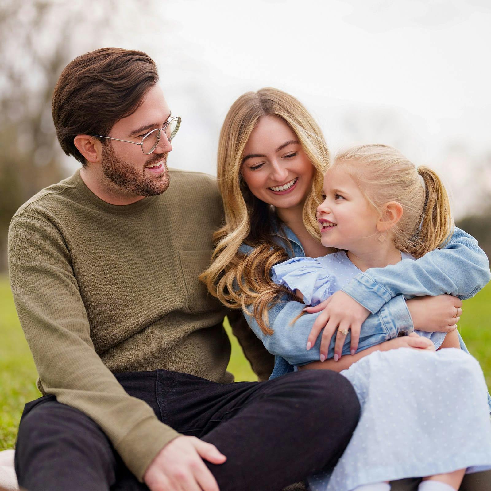 man and woman sitting in a park with a little girl