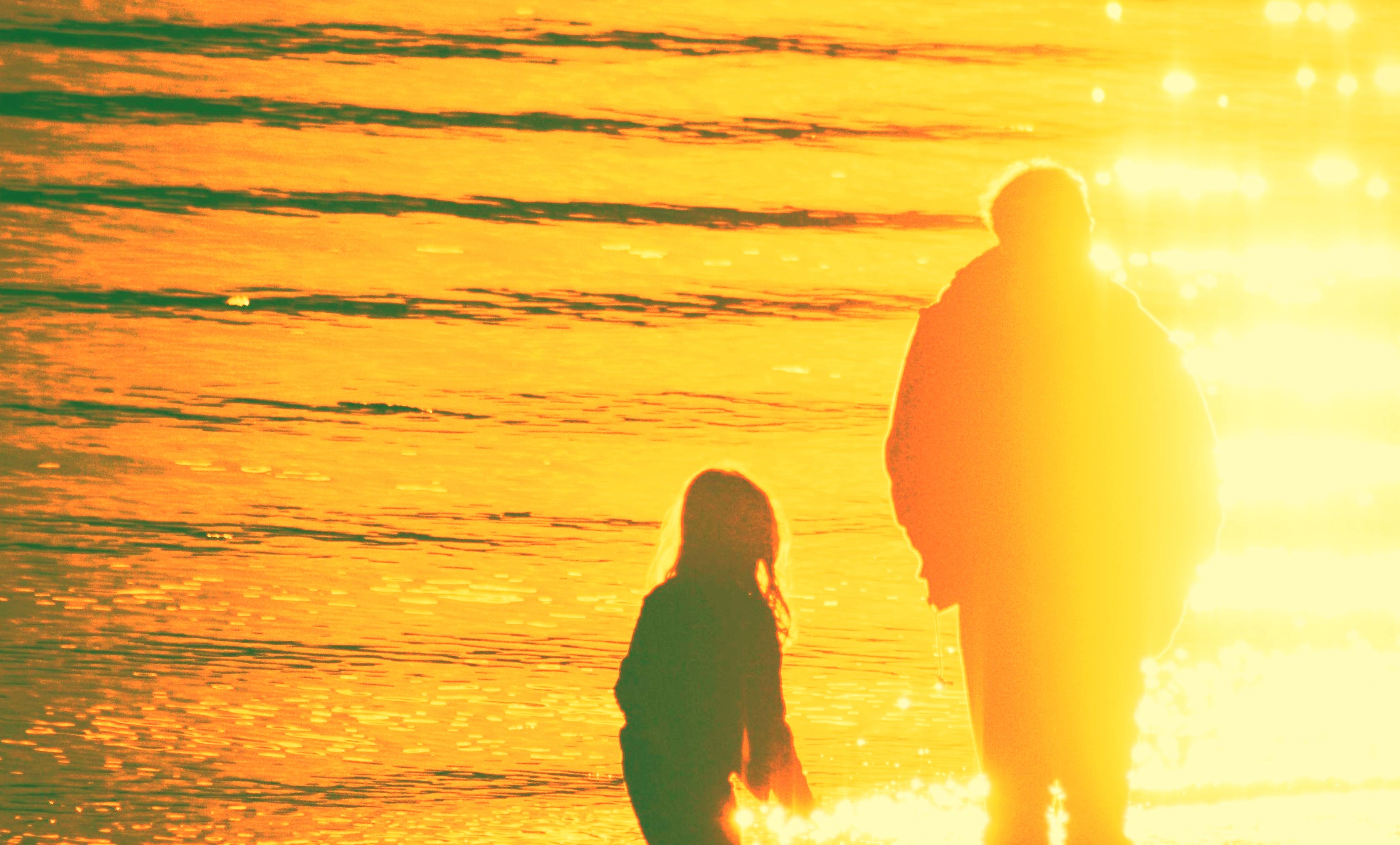 Silhouettes of a person and child walking through warm golden light.