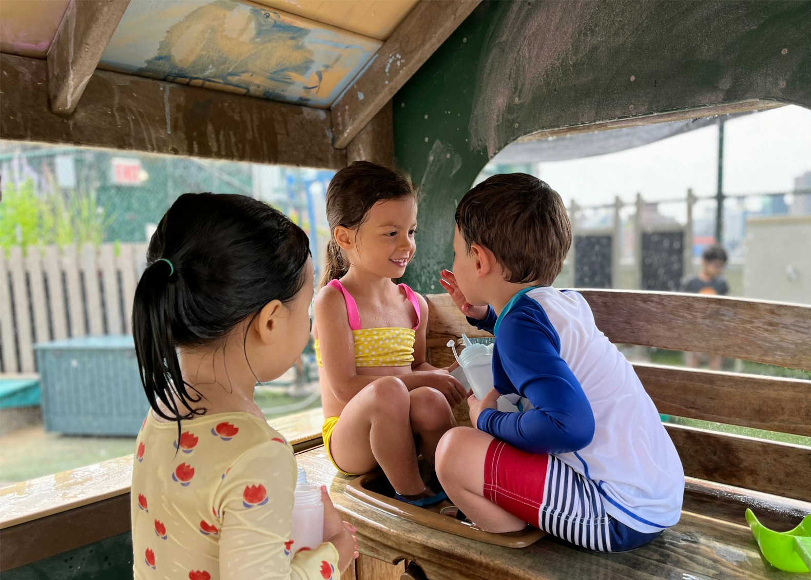 Childern sitting on a park bench, smiling together.