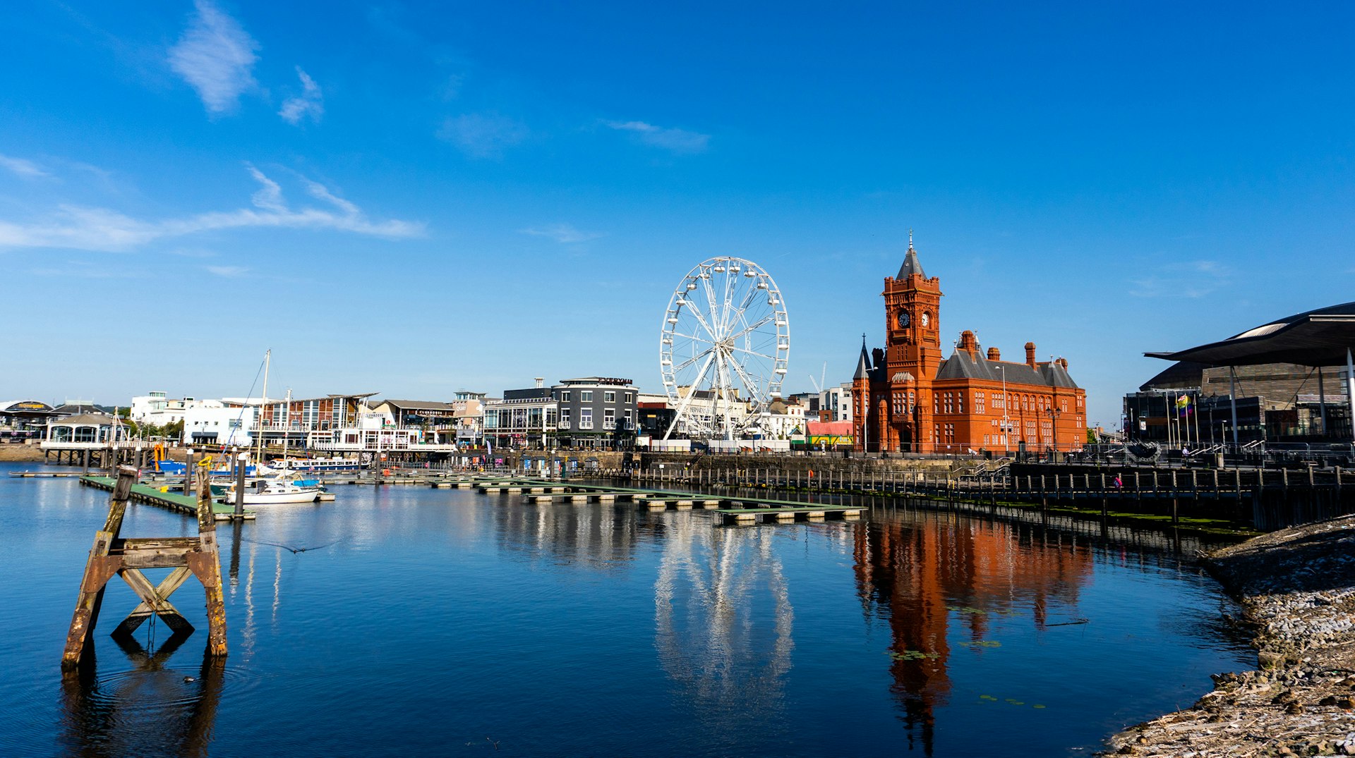 Cardiff Bay waterfront with the Pierhead Building, Ferris wheel, and vibrant marina under a clear blue sky in Wales