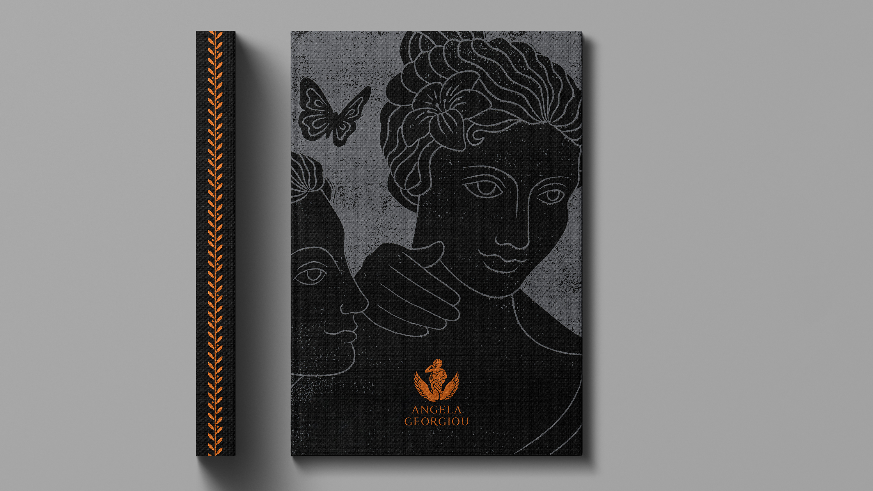 Hardcover fabric book with black and grey Greek goddess illustration, bronze Angela Georgiou logo, and black spine with bronze olive branch pattern
