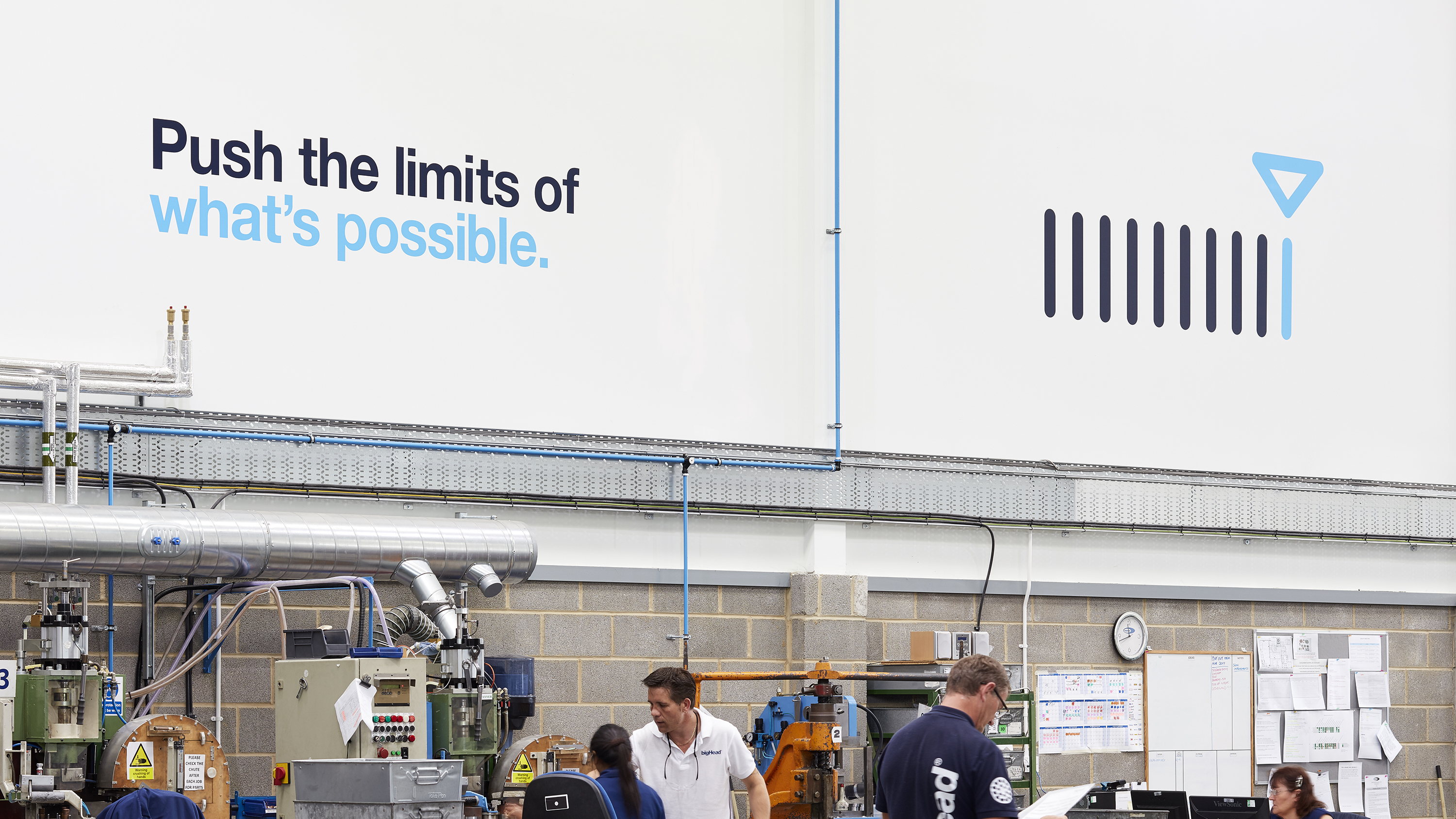 Staff working in bigHead factory with blue and cyan vinyl on wall reading “push the limits of what’s possible” and precision icon