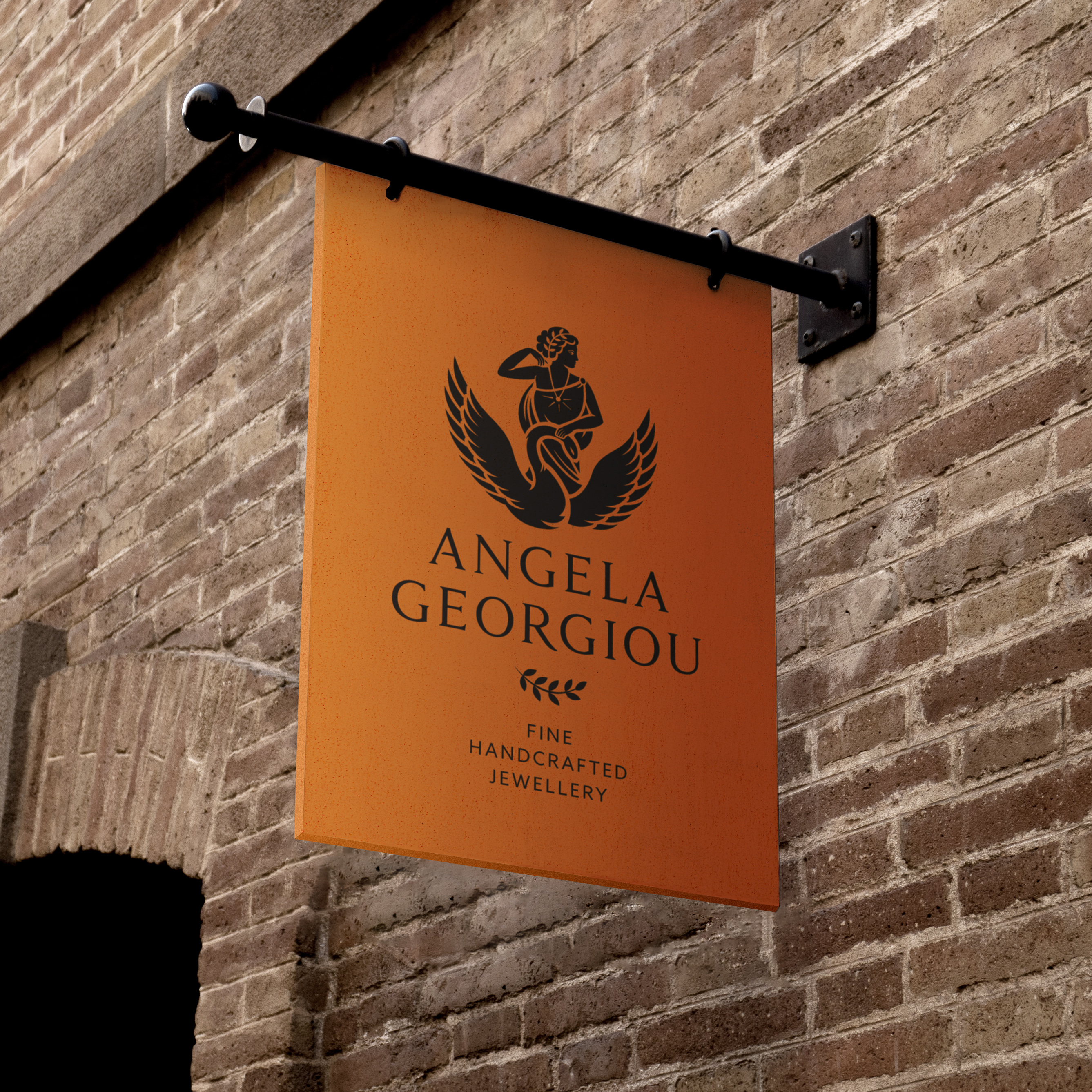 Bronze metal sign on side of red brick building, featuring Angela Georgiou’s Greek mythology inspired logo and strapline: "fine handcrafted jewellery"