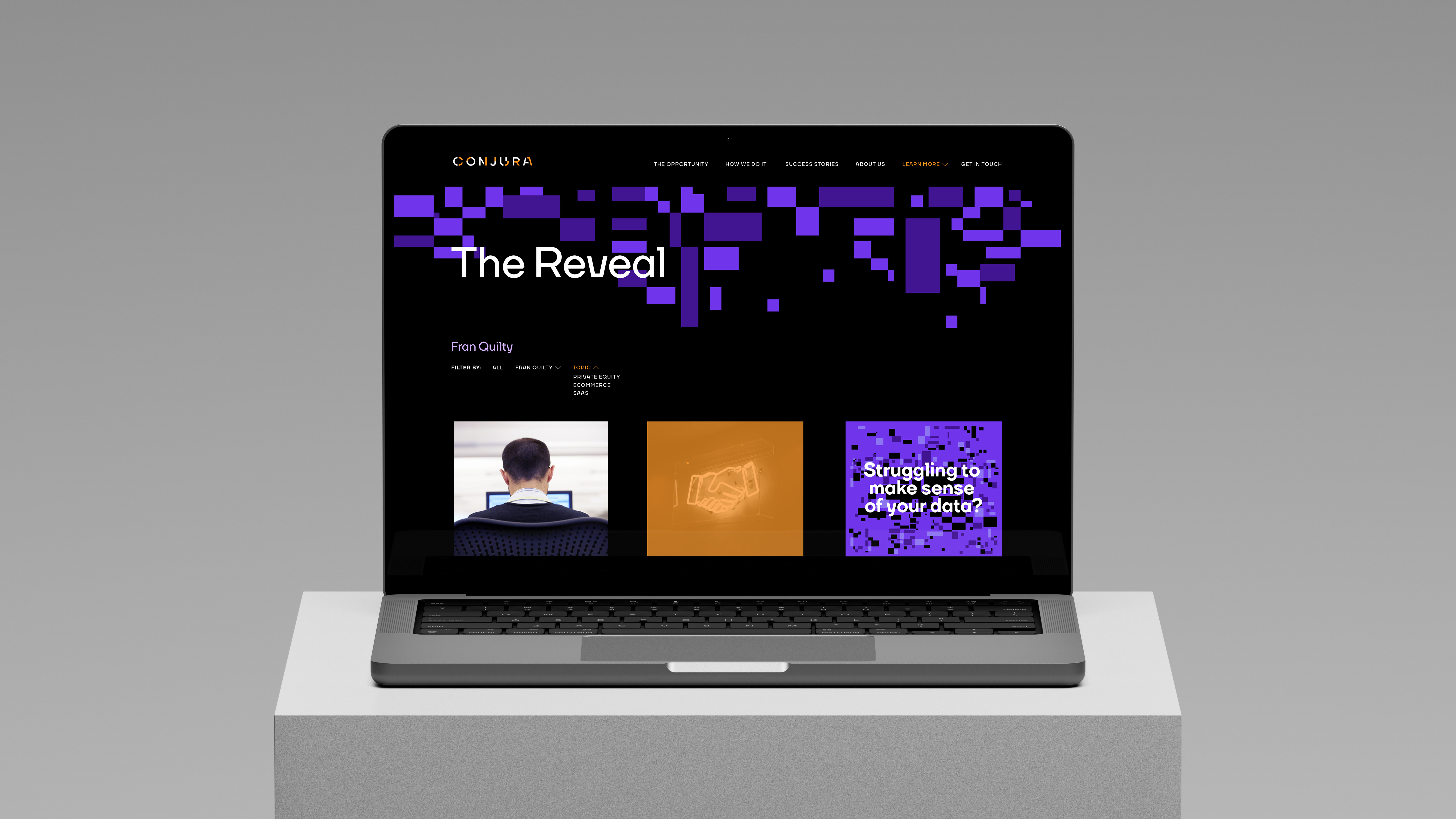 Laptop on light grey block in grey studio setting displaying Conjura’s ‘The Reveal’ webpage with purple pixel design and dark interface