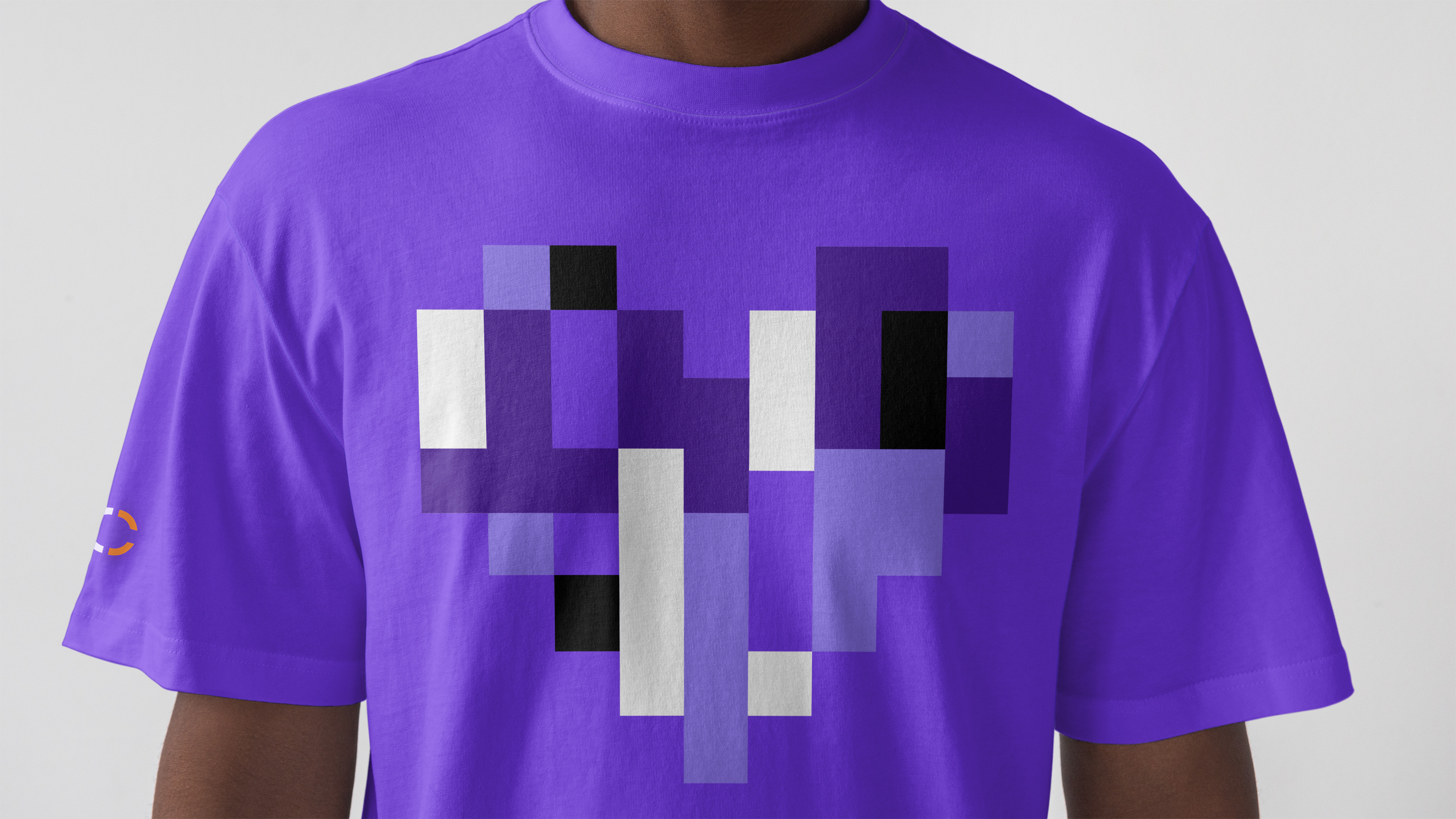 Man wearing purple t-shirt featuring pixel heart design in varied purple shades and black and white, with Conjura logo symbol on right sleeve