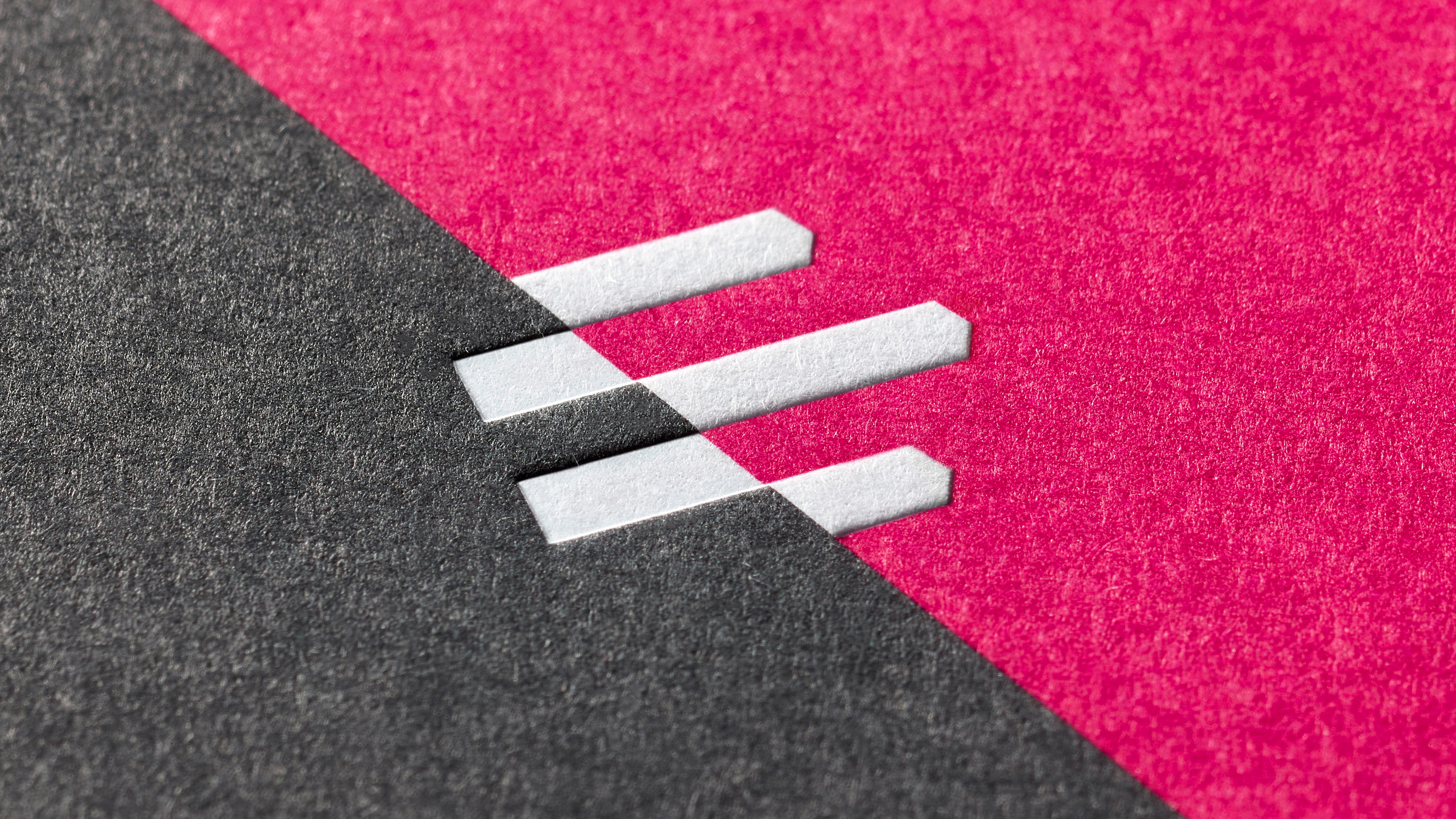 Close-up of white Emergence logo embossed and debossed on pink and dark grey paper