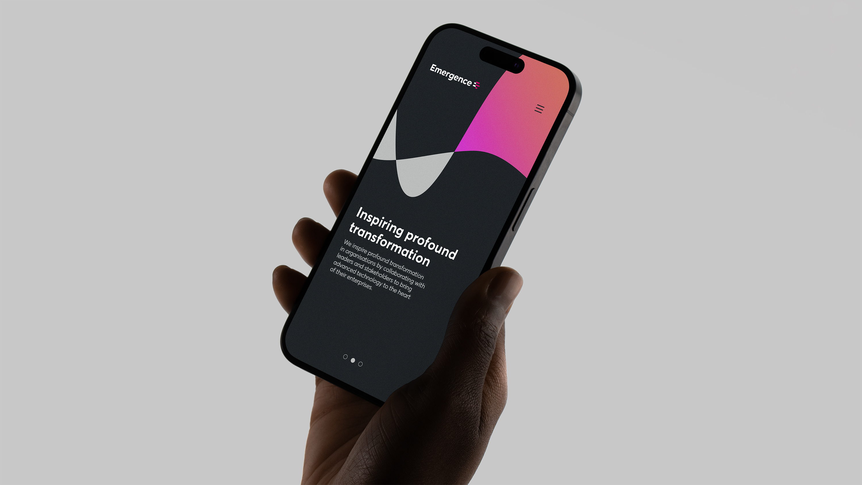 Hand holding smartphone showing dark grey Emergence website with abstract colourful shapes and text 'Inspiring profound transformation’