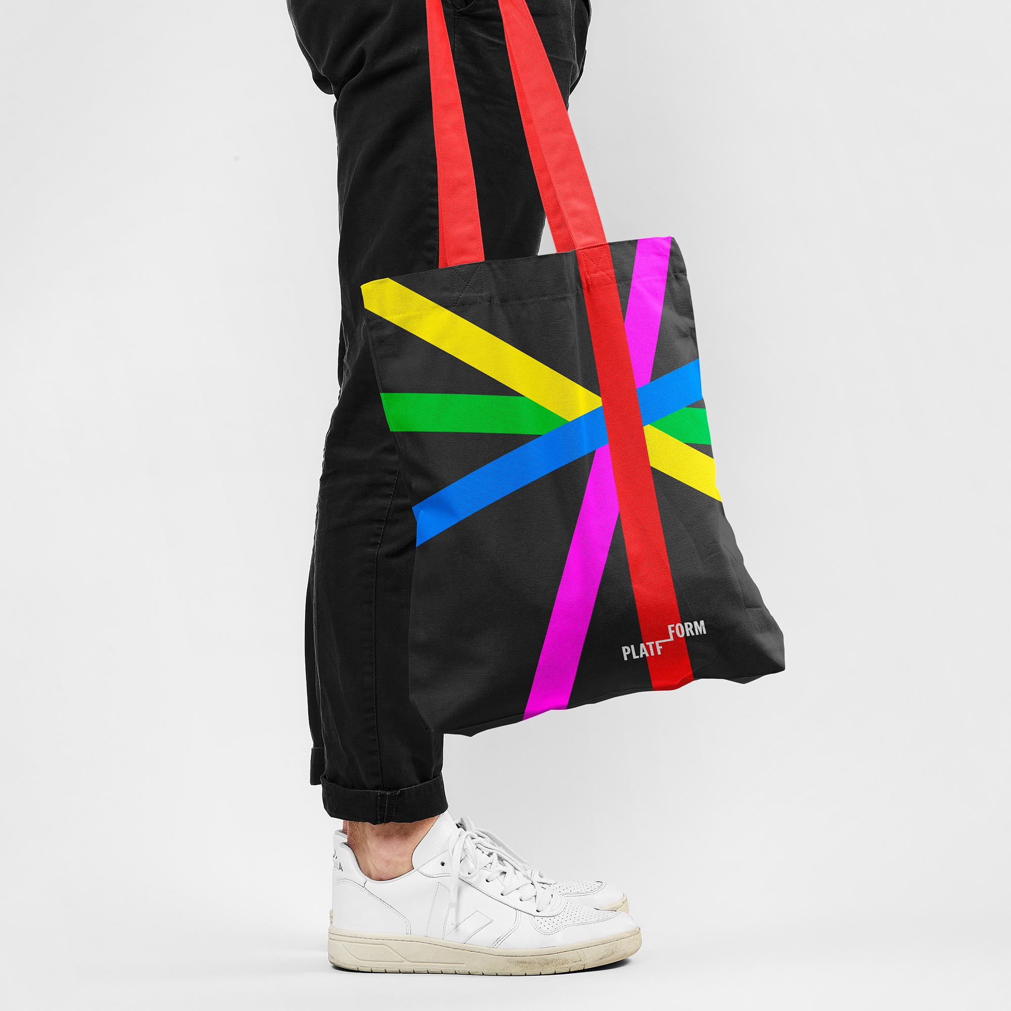 Man in black trousers and white trainers holding black tote bag with red straps, bold line graphics and Platfform logo