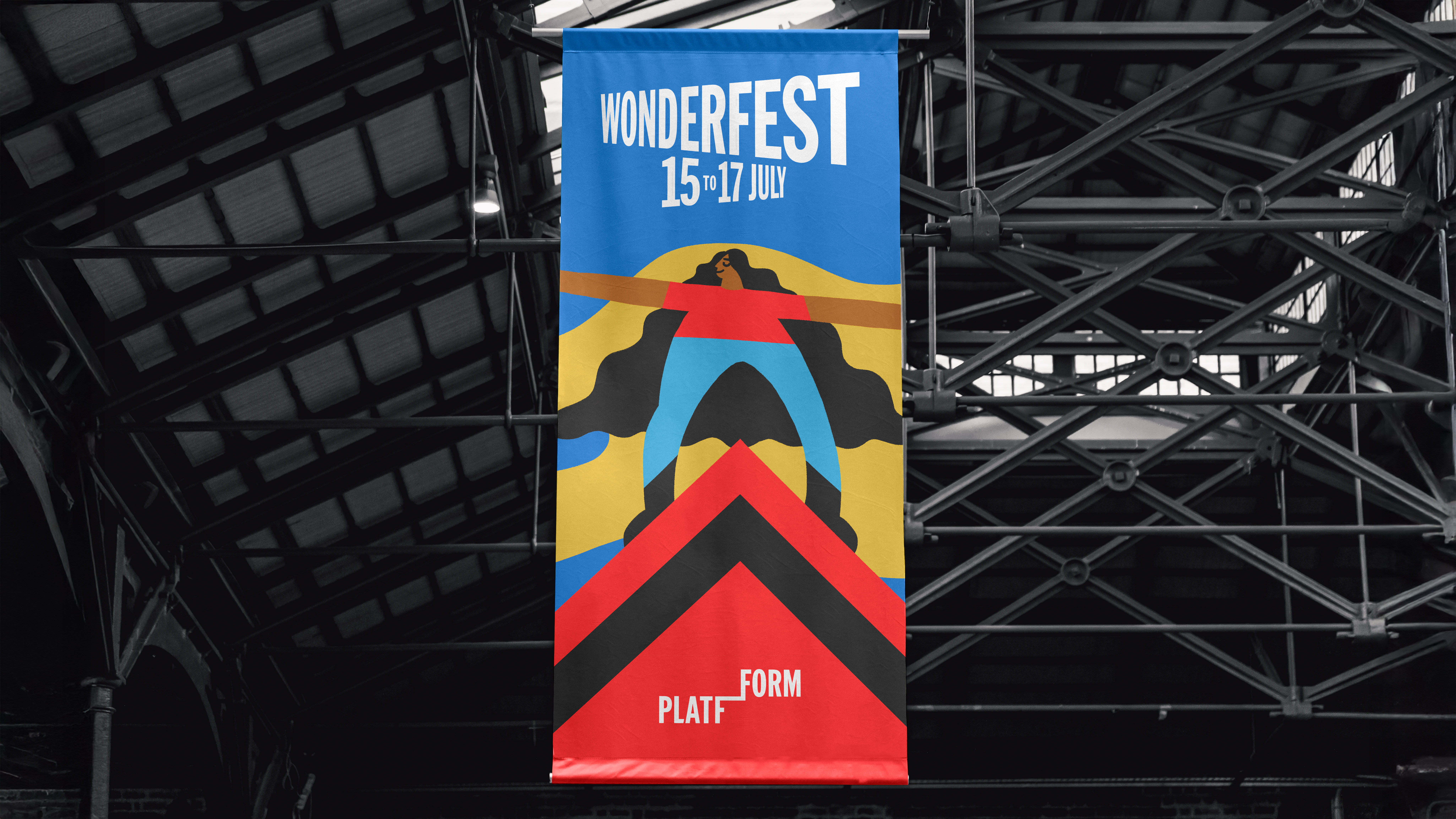 Vertical banner hanging in a warehouse advertising Wonderfest event with colourful friendly illustration of woman standing on a mountain peak
