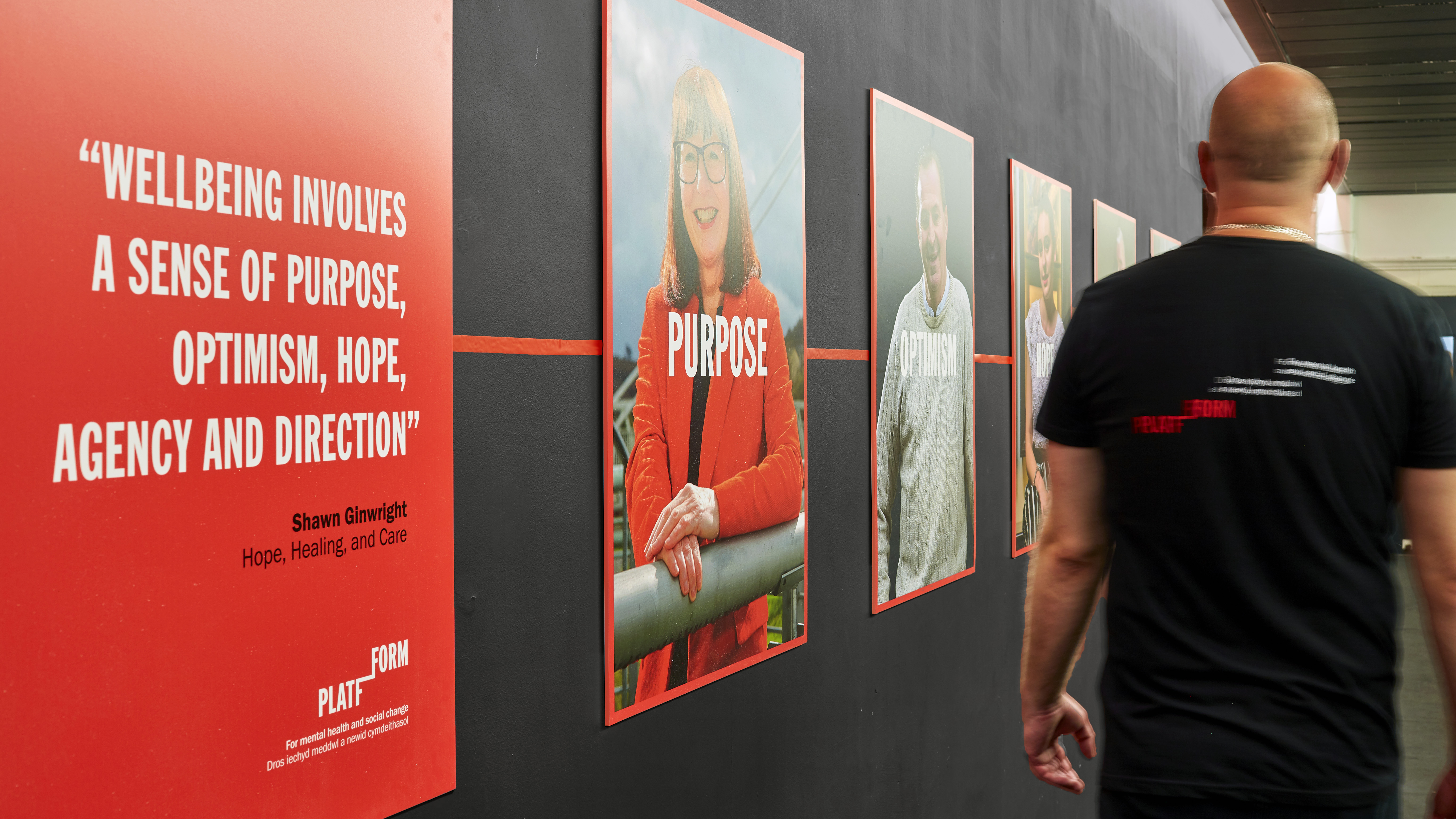Man wearing Platfform T-shirt walking past gallery wall of photos and stories of people the charity has supported