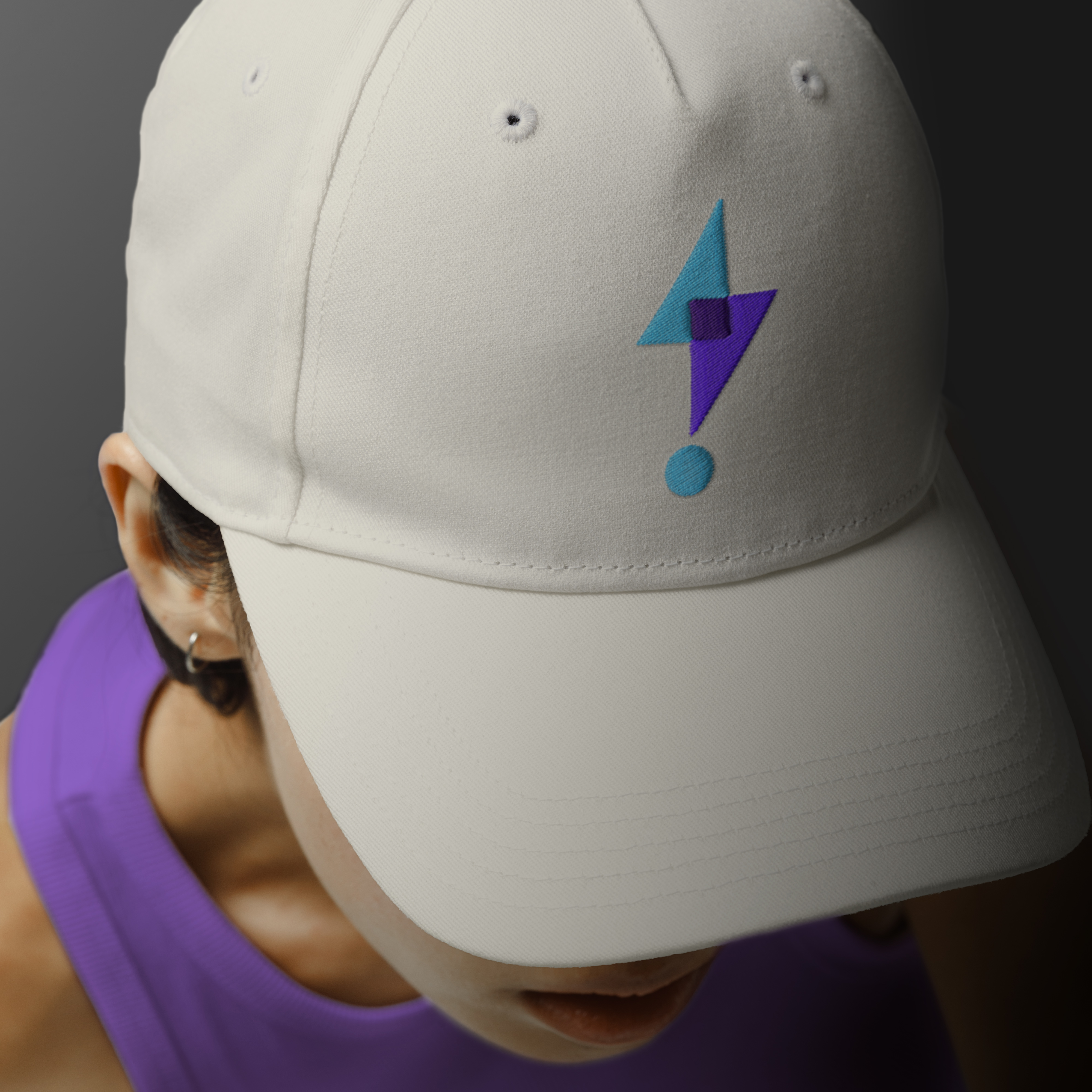 Top view of woman in purple tank top and cream hat with abstract blue and purple lightning bolt embroidered graphic, shot against dark grey backdrop