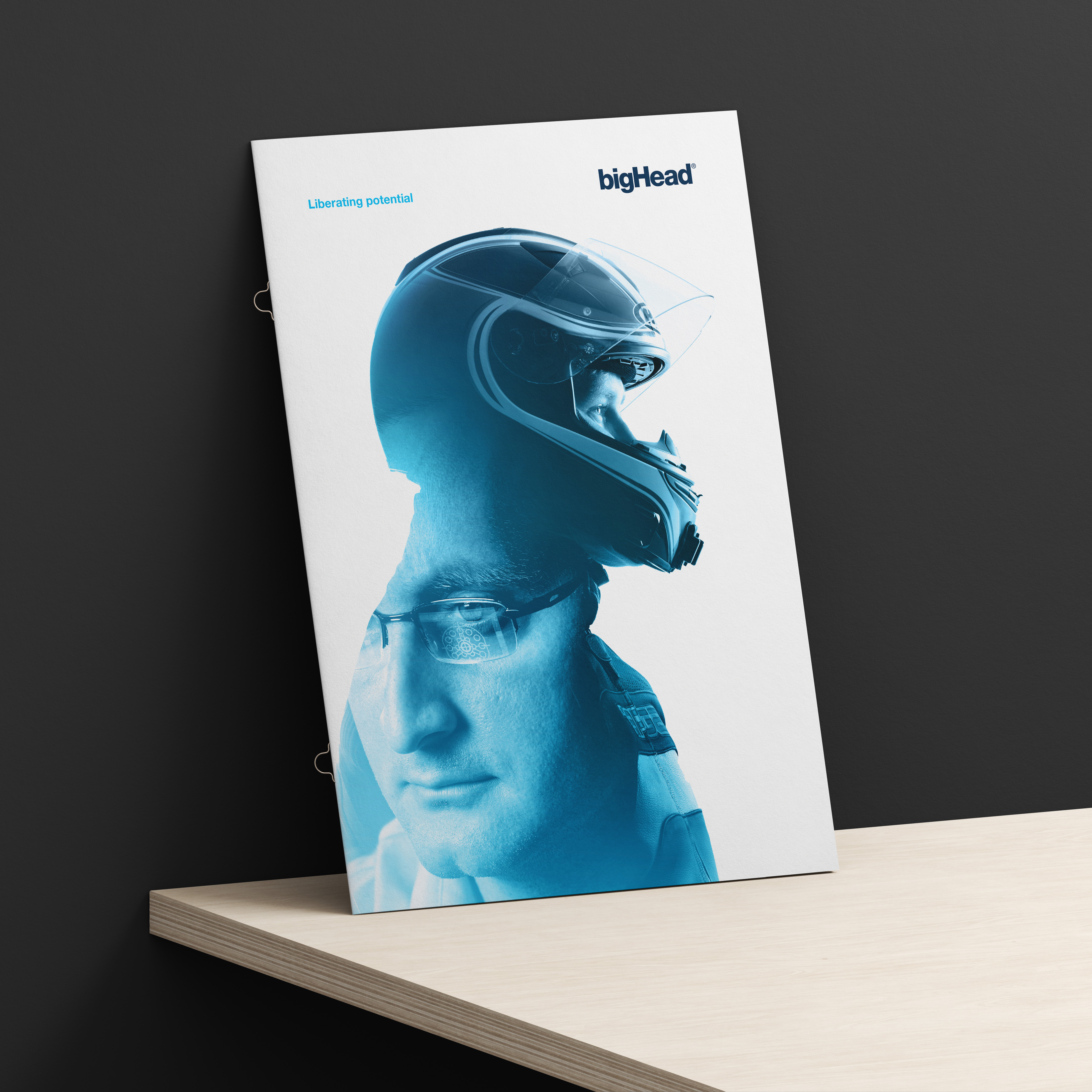White brochure cover featuring blue double-exposure image race car driver and bighead engineer, with logo and strapline, leaning against dark wall