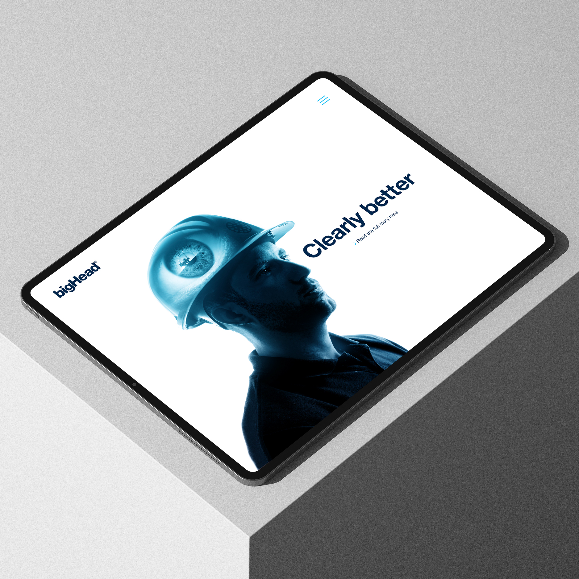 iPad on grey surface showing bigHead webpage with blue double exposure of engineer and eye alongside logo and words "clearly better" in dark blue