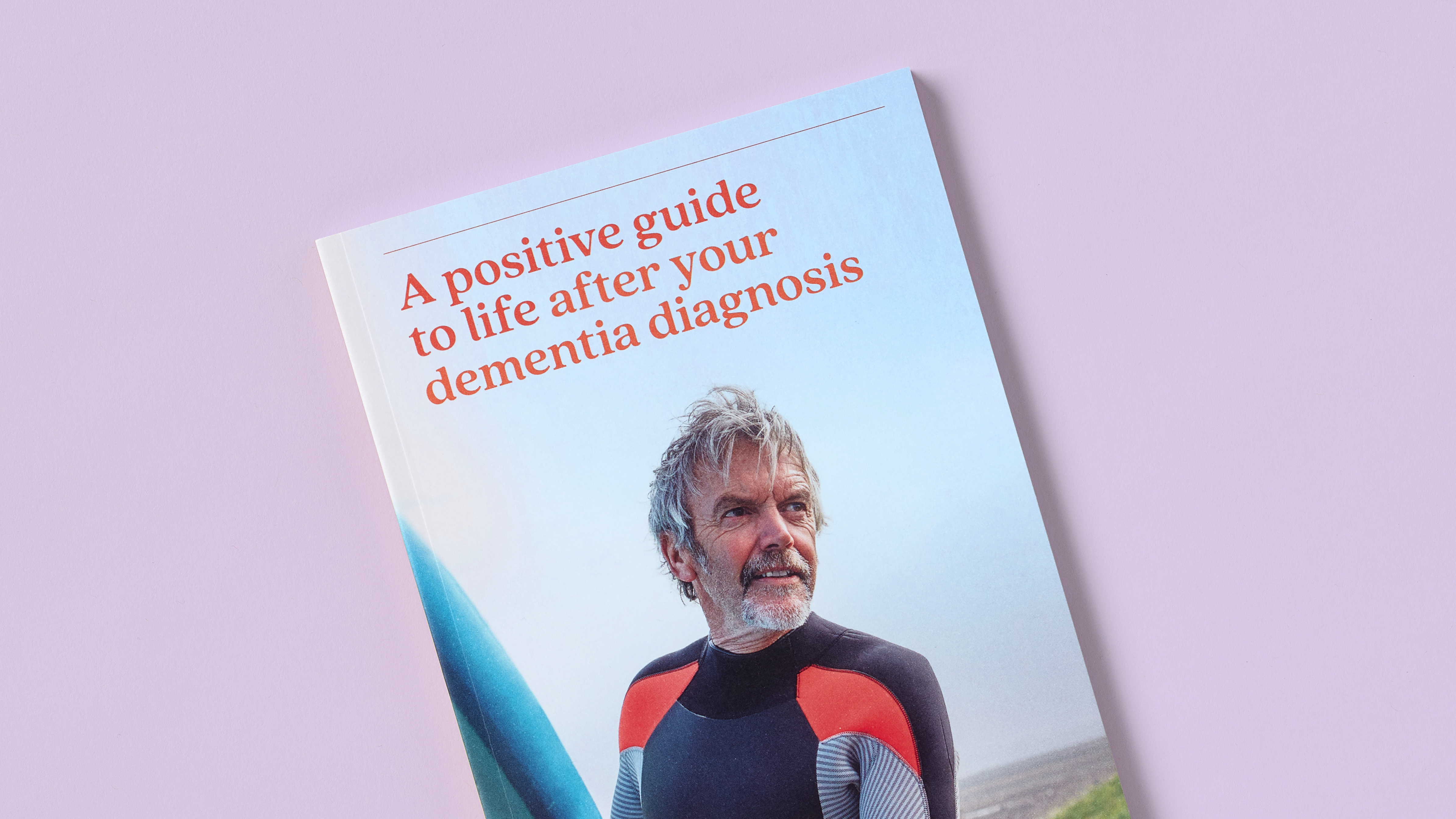 Close-up of dementia guidebook cover showing older man in surfing gear with soft red title on light pink background