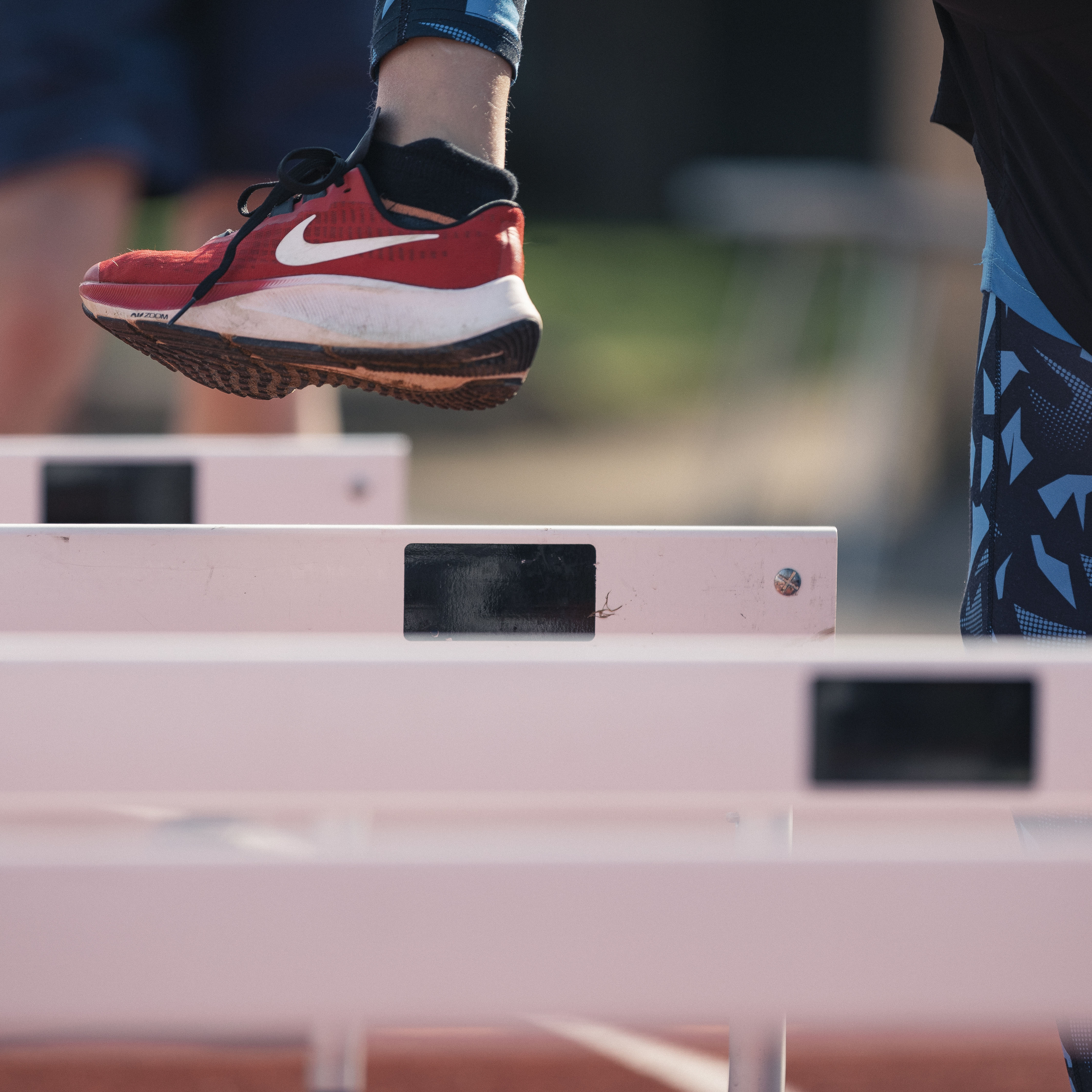 Close-up of child participating at track and field, focusing on red trainer stepping over white hurdles