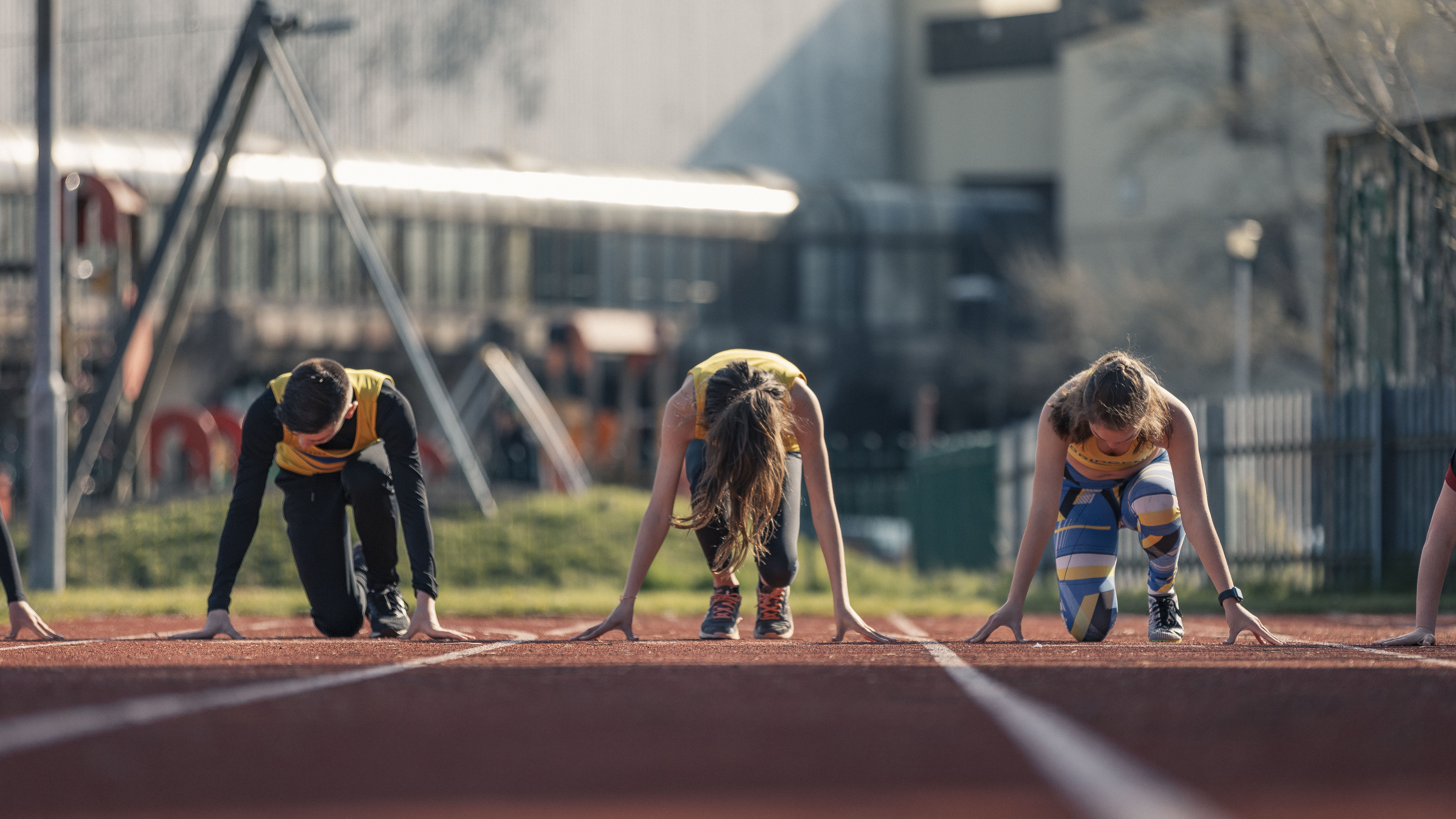 Front view of three children in starting positions on running track preparing for race on sunny day