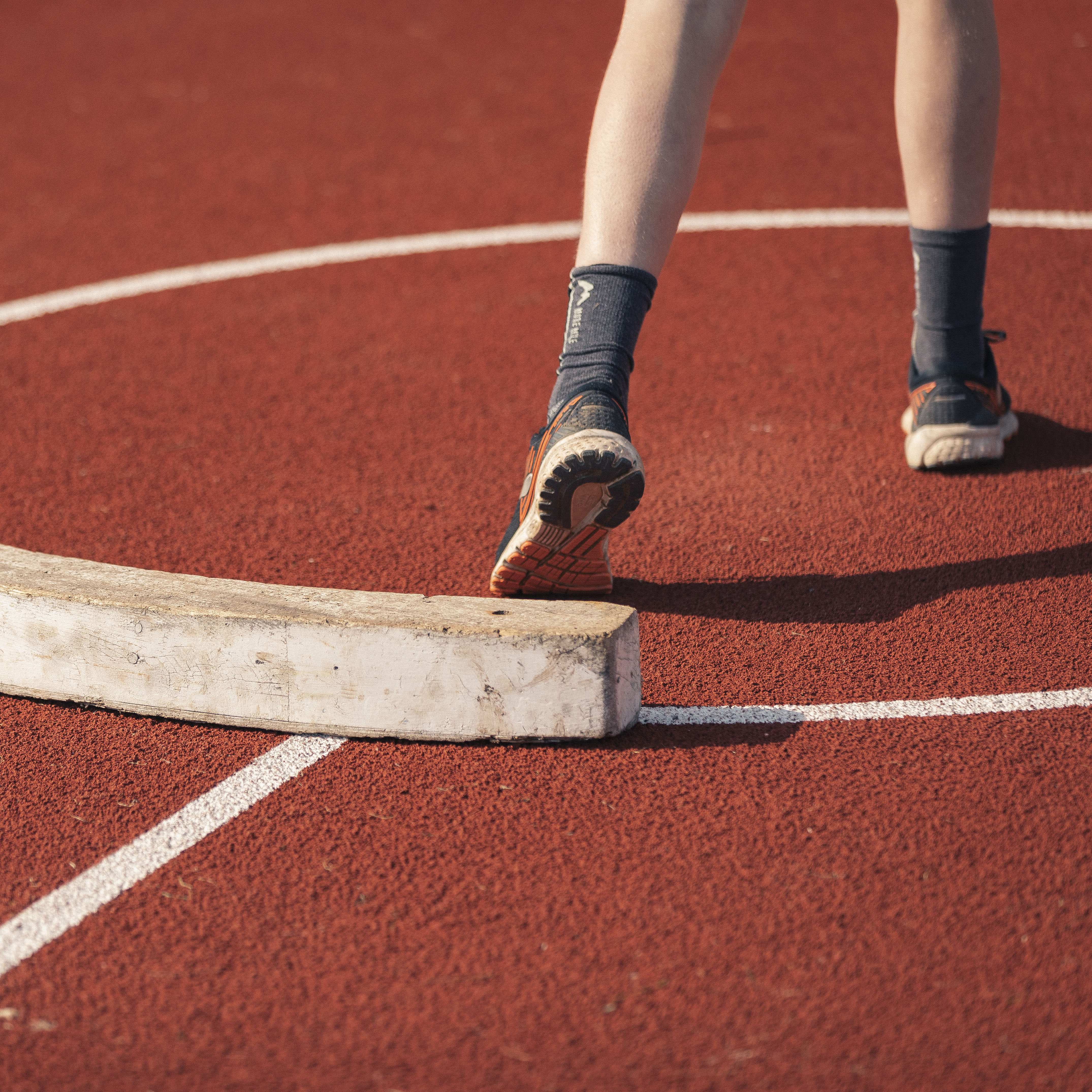 Back view of child’s legs in starting position for track and field event on red and white floor