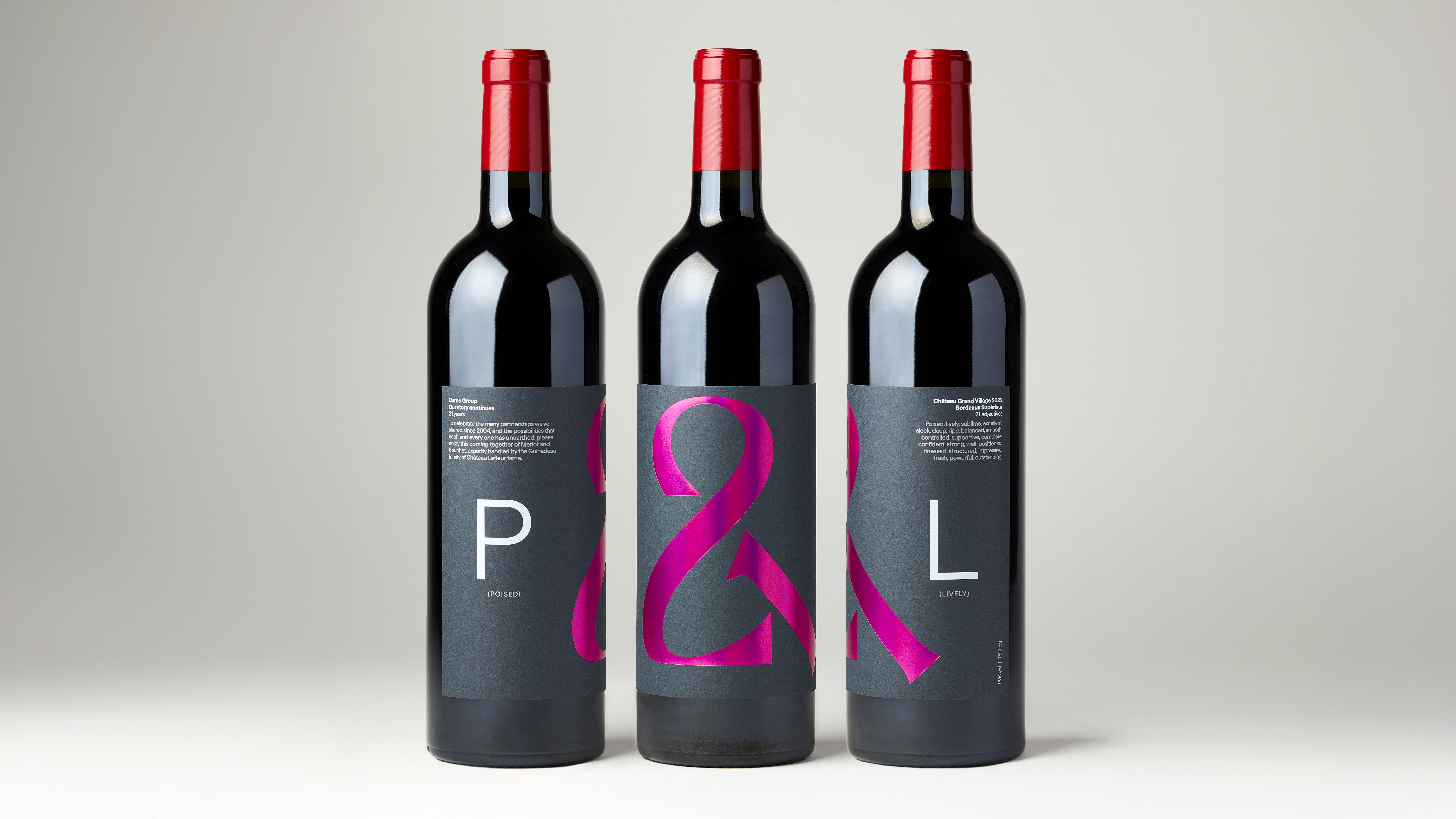 Studio shot of three red wine bottles with P&L label, holographic hot pink foiled ampersand logo, and white text on dark grey