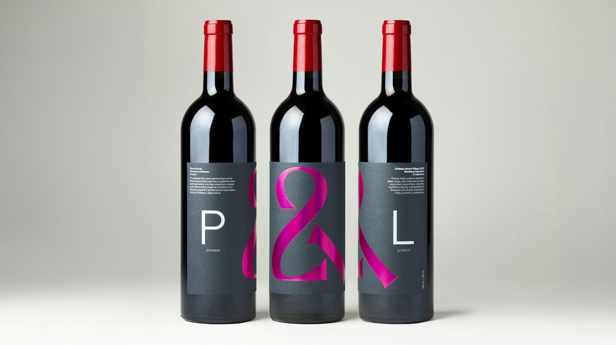 Studio shot of three red wine bottles with P&L label, holographic hot pink foiled ampersand logo, and white text on dark grey