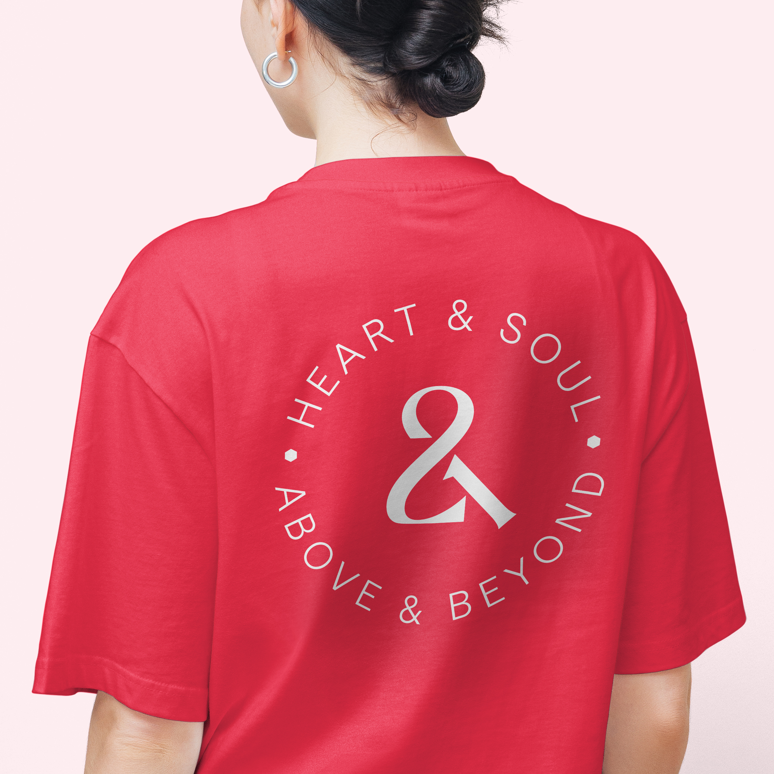 Back of woman wearing coral tshirt with white roundel logo reading "heart & soul, above & beyond" for company 21st anniversary