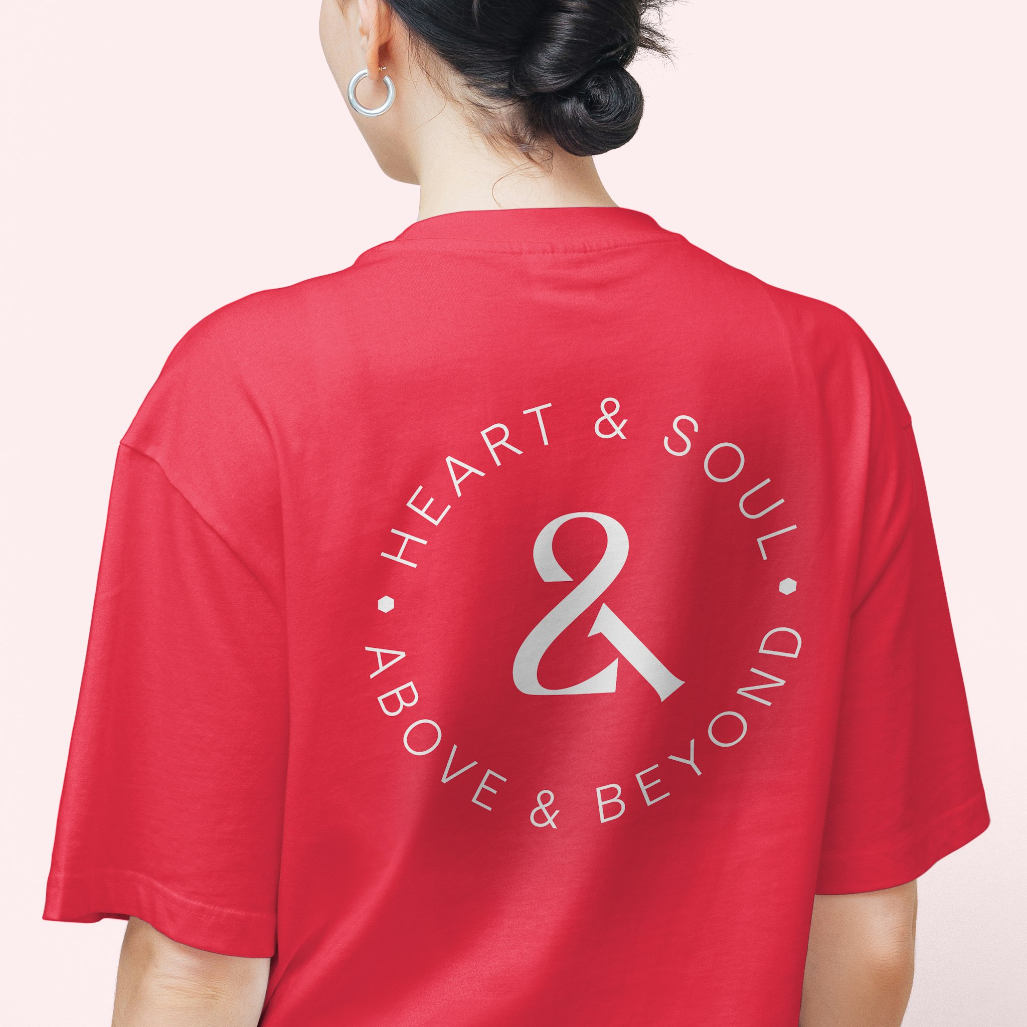 Back of woman wearing coral tshirt with white roundel logo reading "heart & soul, above & beyond" for company 21st anniversary