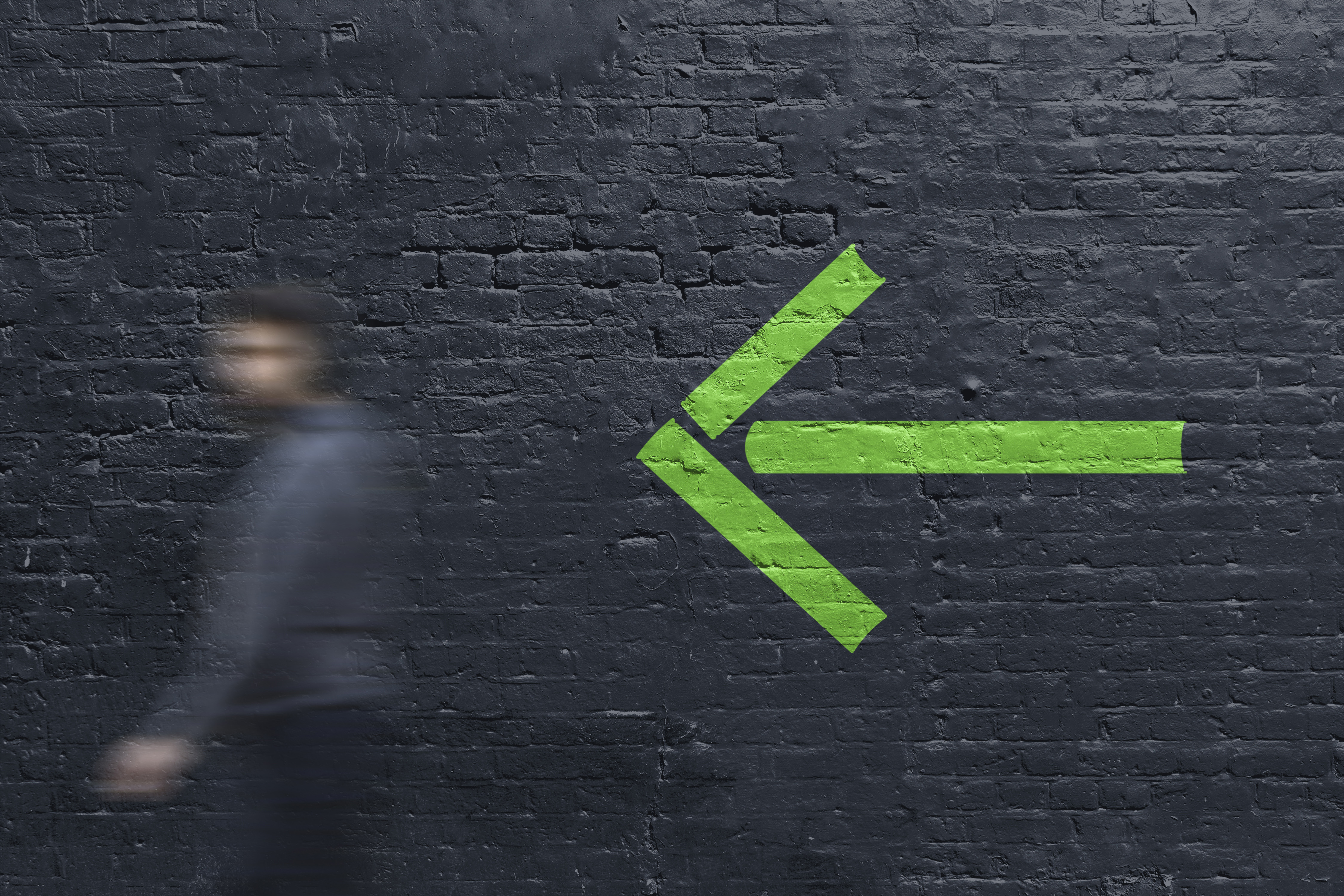 Man walking past dark grey painted brick wall with bright green wayfinding arrow graphic formed from book spine shapes