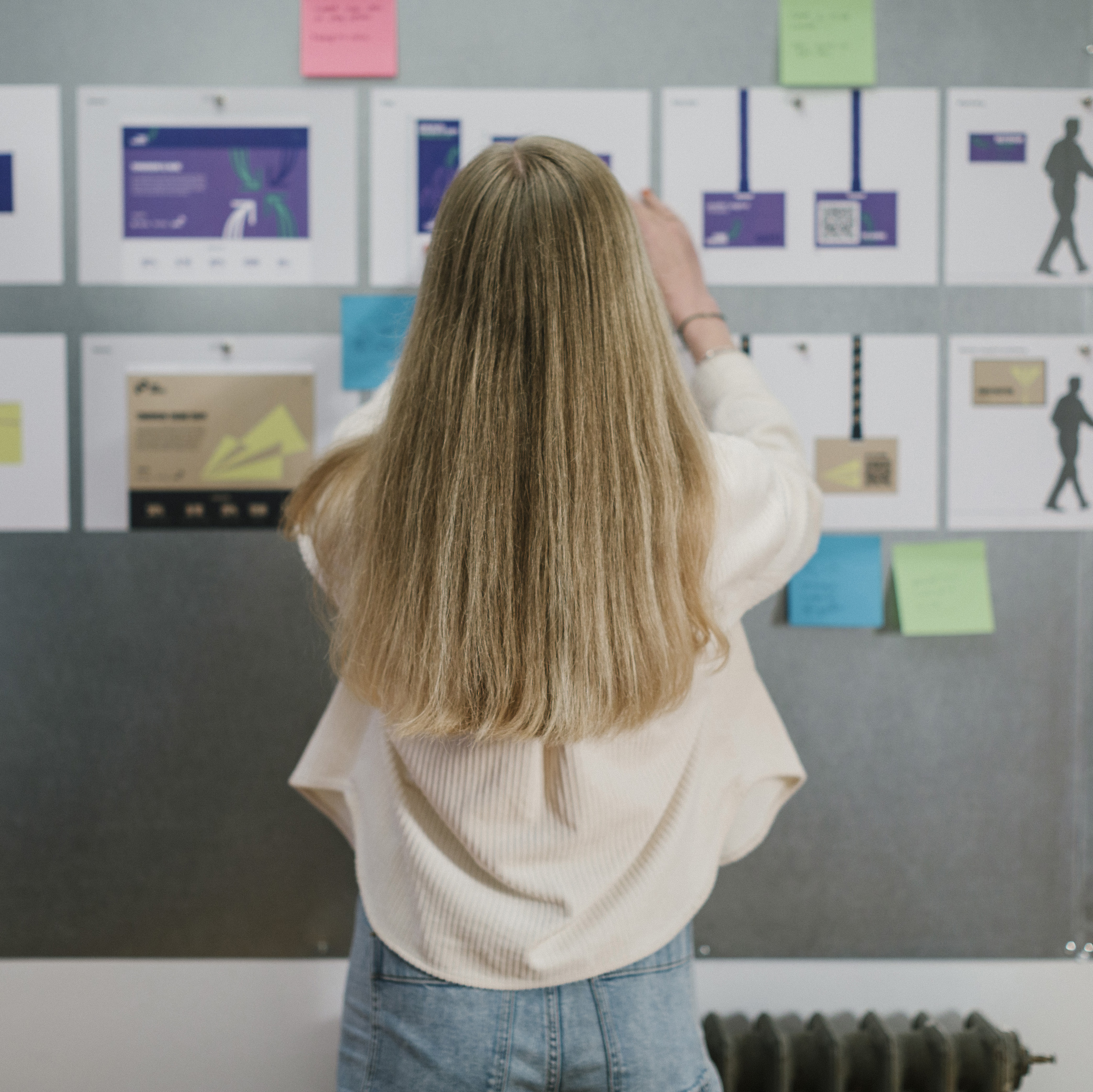 Woman brainstorming and organising design ideas on wall with creative project notes and mockups