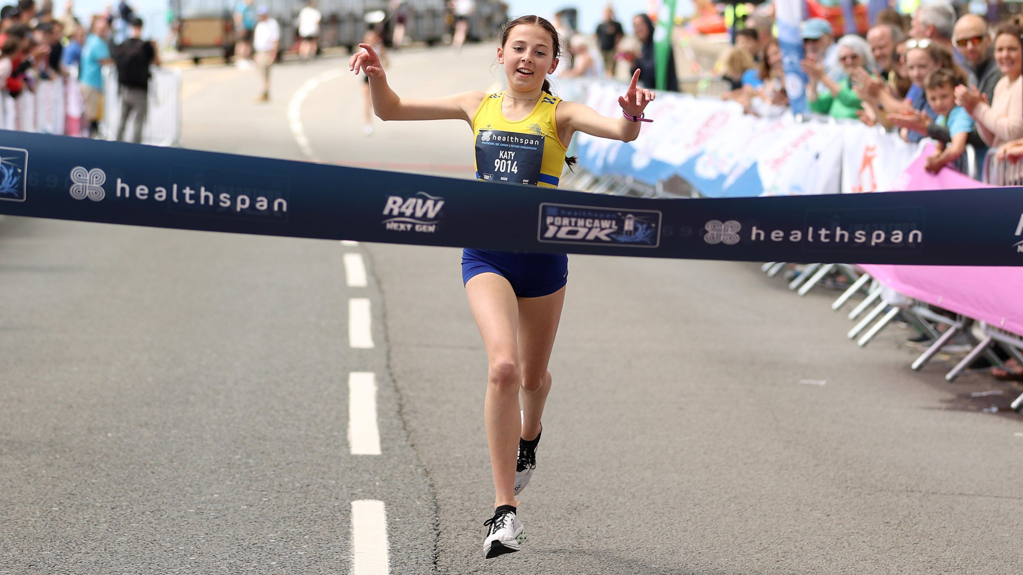 Excited young girl in running kit approaching finish line at Porthcawl 10K with cheering crowd