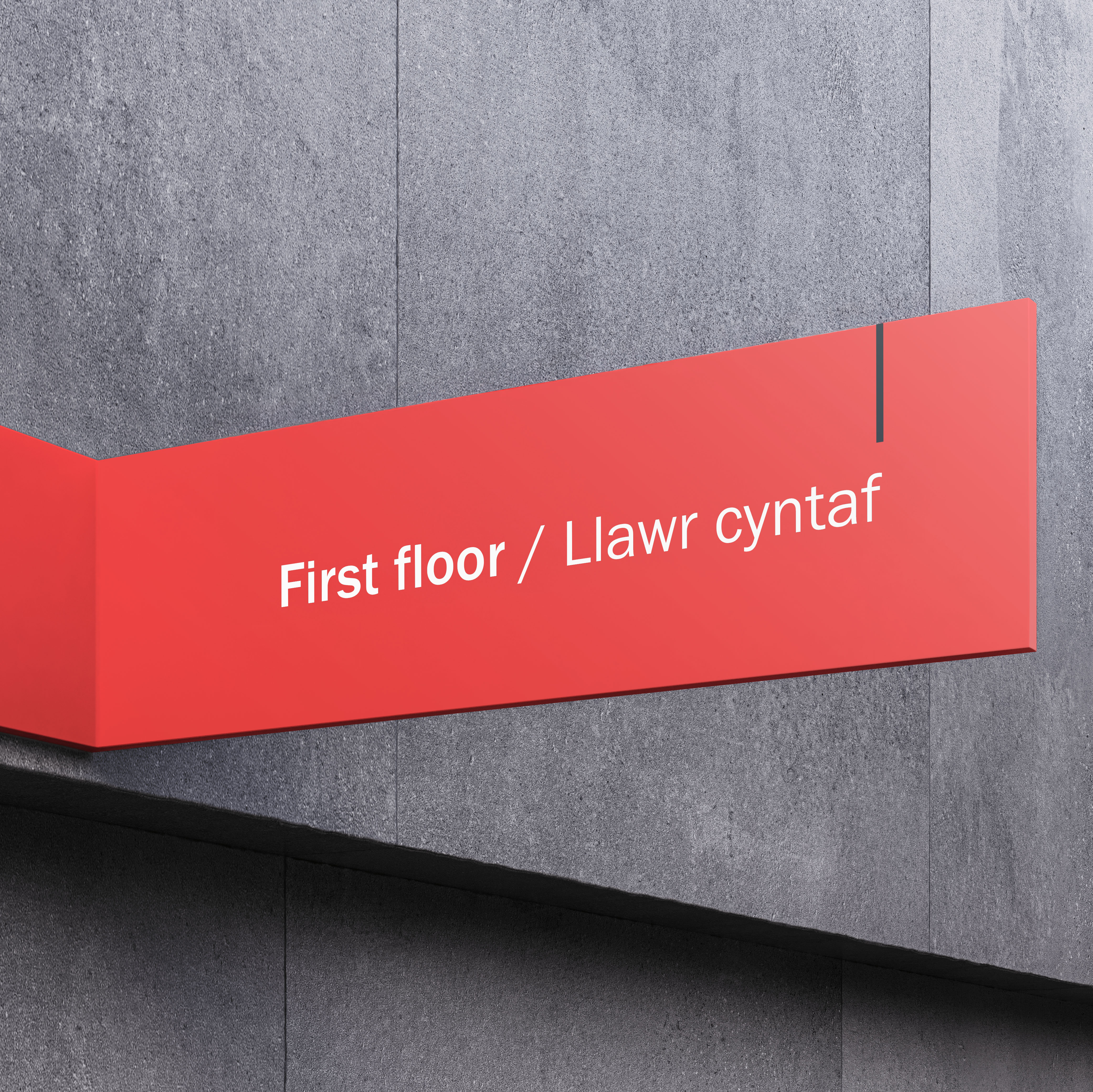 Red first floor sign with white text mounted on grey stone wall of modern building