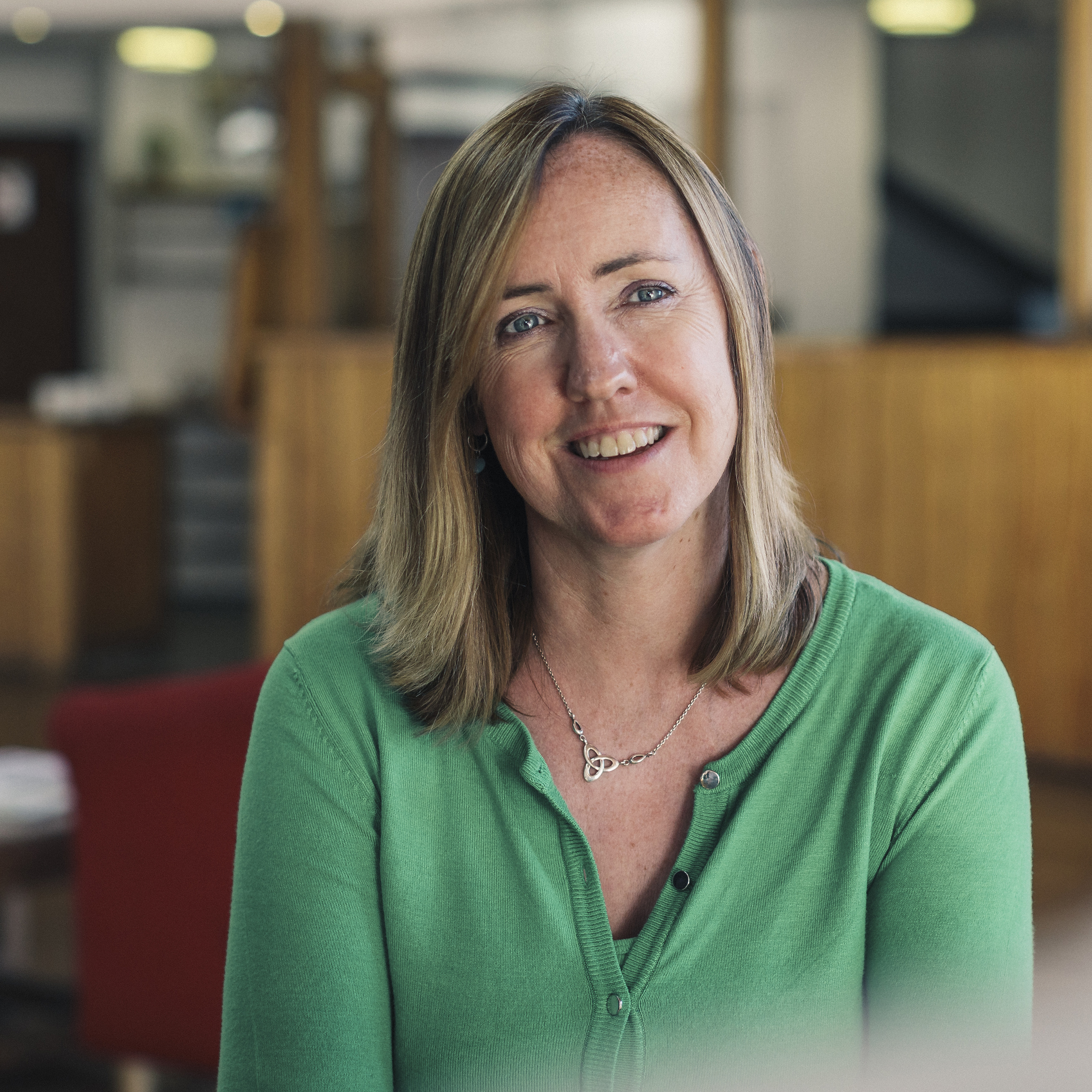 Smiling professional woman in green cardigan at modern design studio workspace