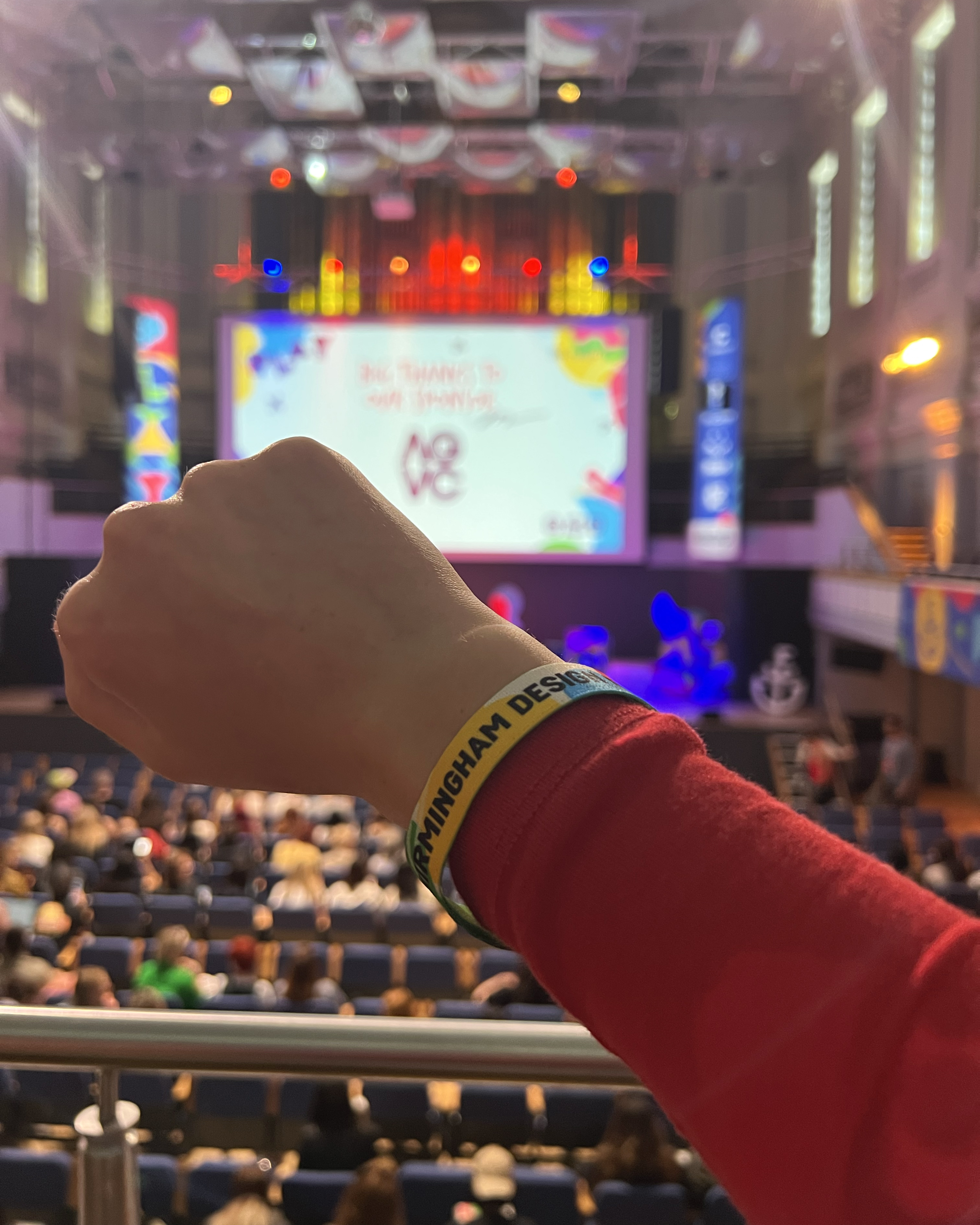 Attendee wearing event wristband with Birmingham Design Festival 2025 stage in the background, highlighting festival experience