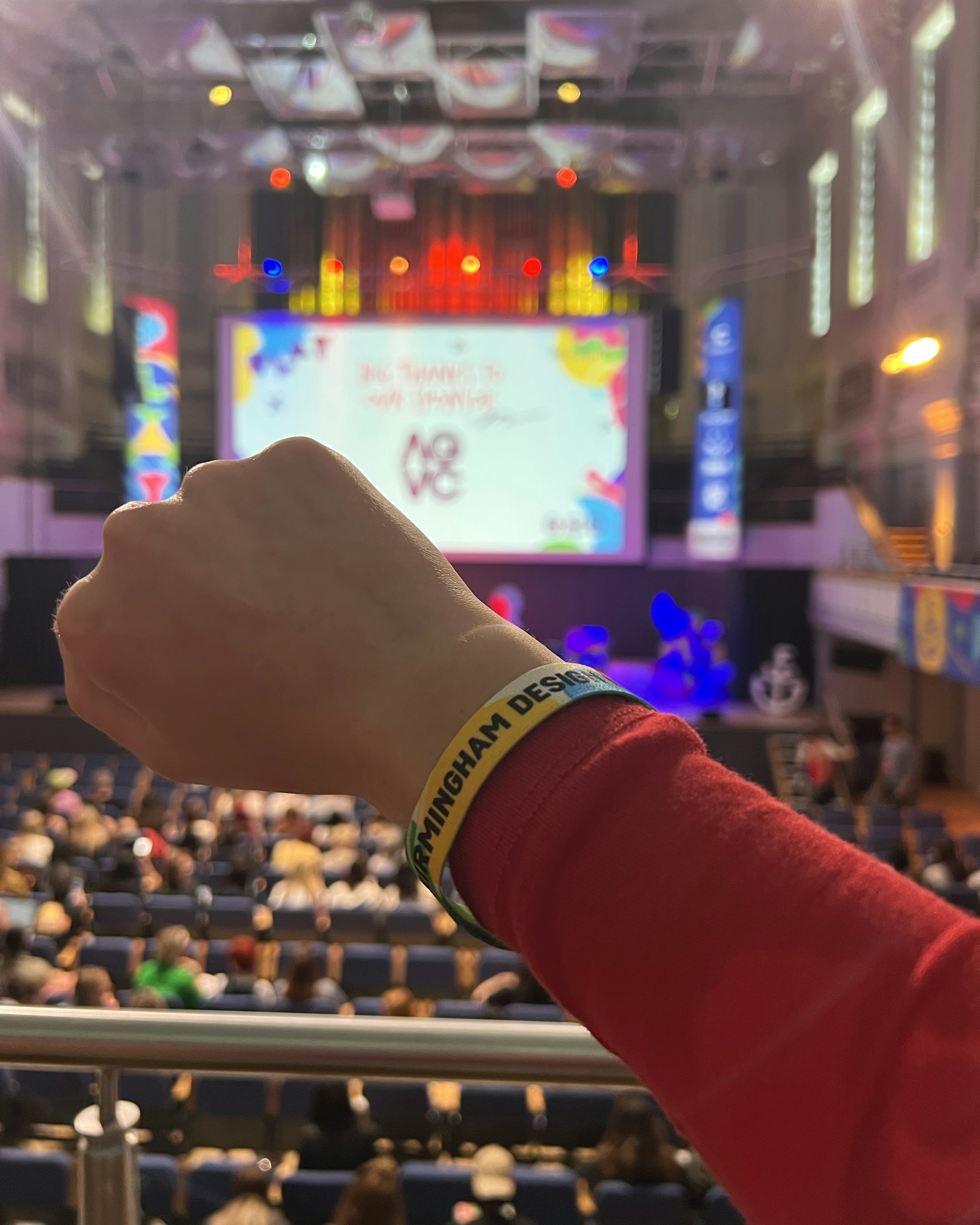 Attendee wearing event wristband with Birmingham Design Festival 2025 stage in the background, highlighting festival experience
