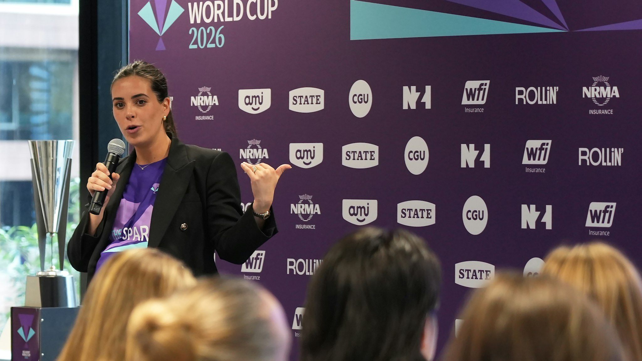 Woman speaking to audience beside silver trophy in front of IAG branded sponsor backdrop